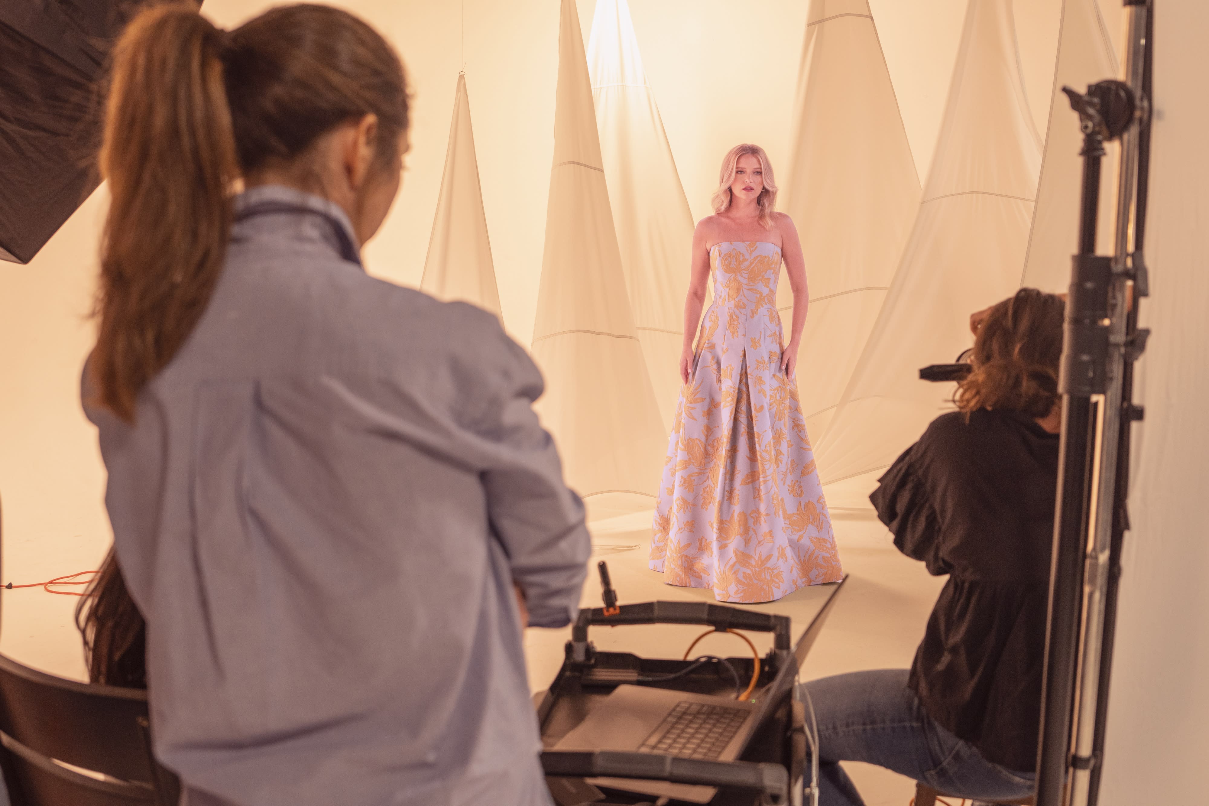 A group of women is posing around a luxury car during a video shoot in a studio setting.