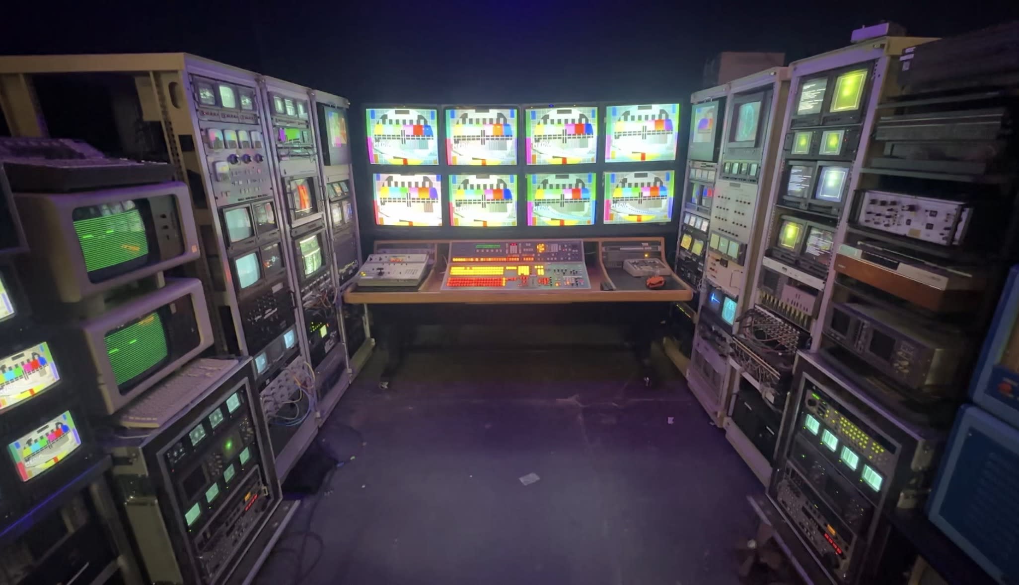 A model poses dramatically by a vintage control panel surrounded by an array of retro monitors and lights.