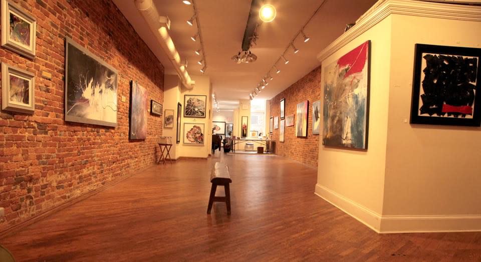 The image shows an art gallery with a wooden floor and exposed brick walls, where guests are gathered for a bridal shower celebration.