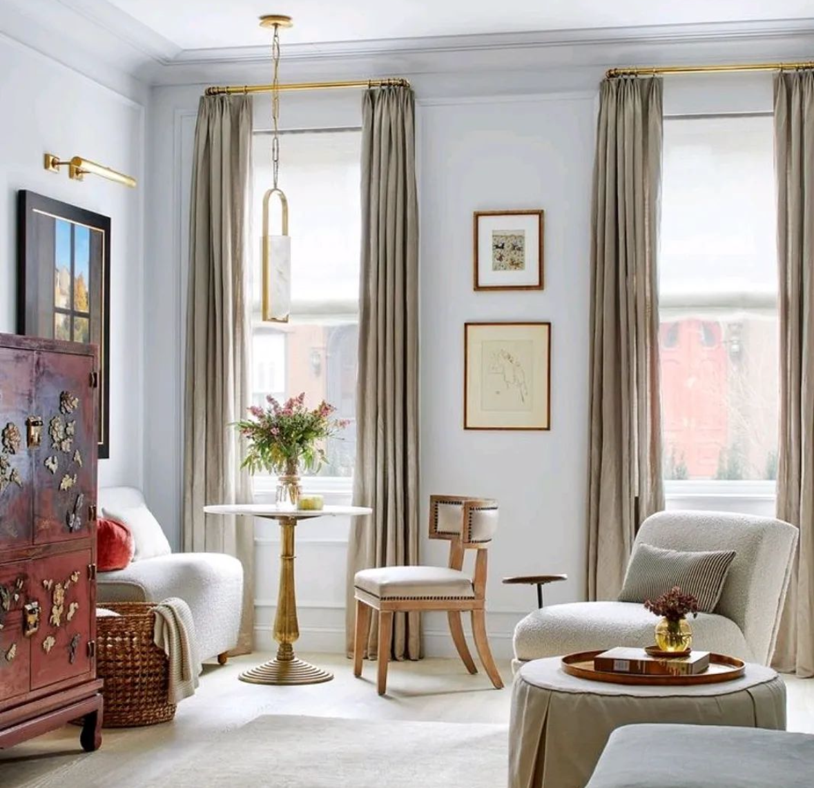 A bedside table holds a lit lamp and a vase with flowers next to a neatly made bed.