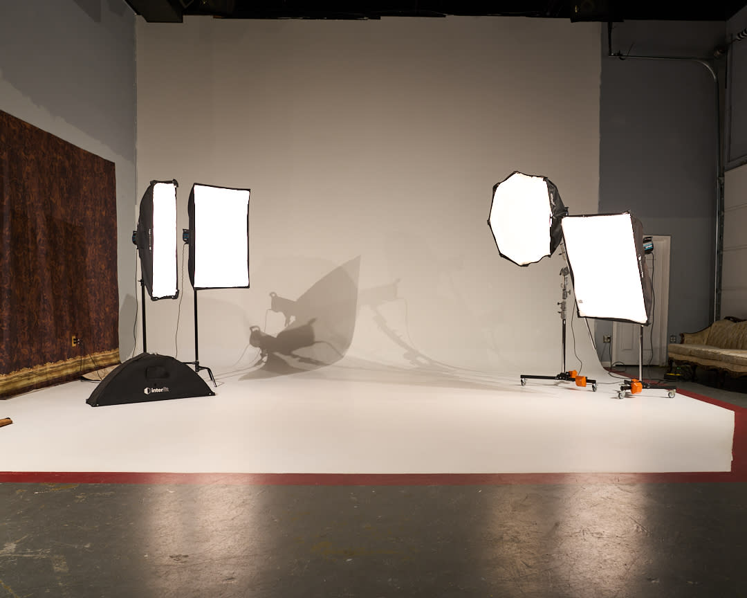 A musician poses on a vintage sofa in a studio during a video shoot, with an electric guitar displayed behind him.