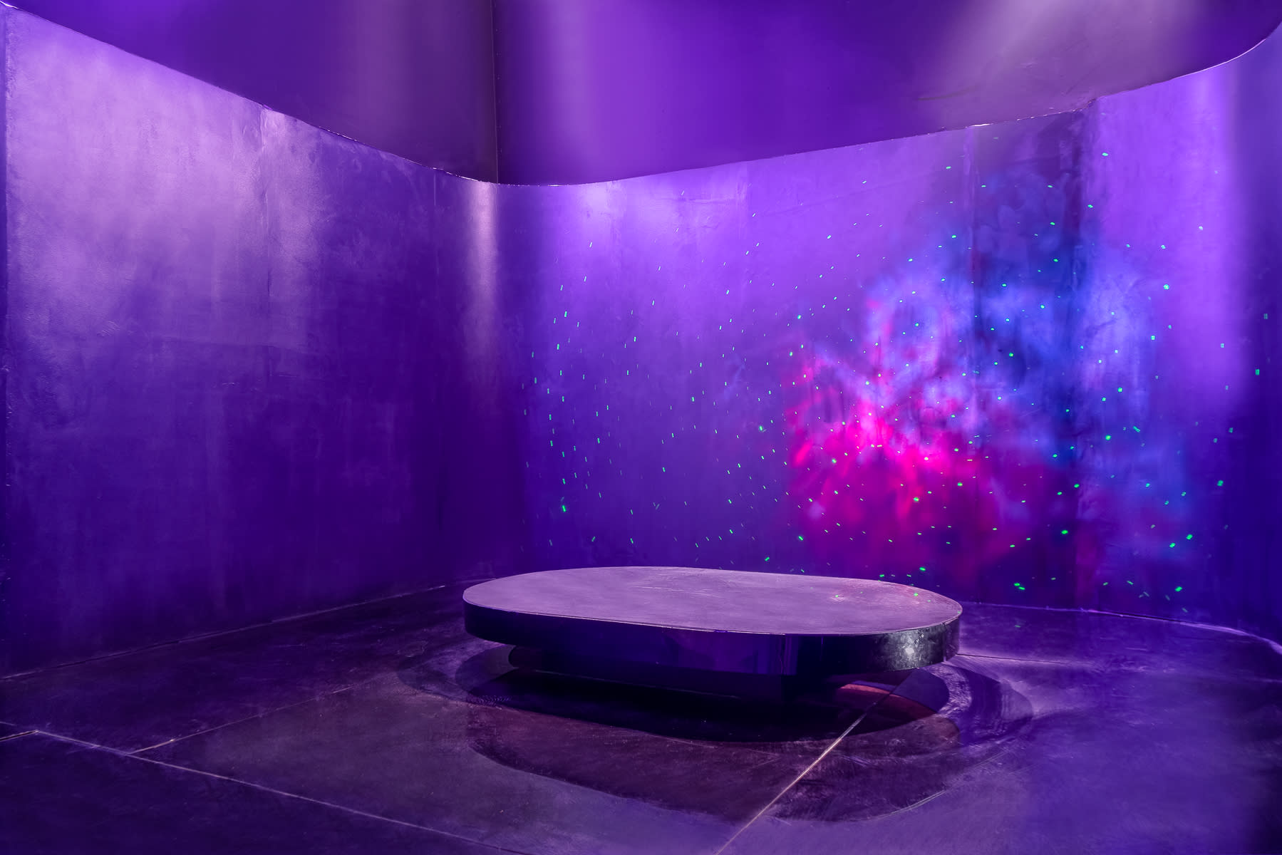 A performer kneels on a circular stage while striking a dynamic pose under purple lighting.