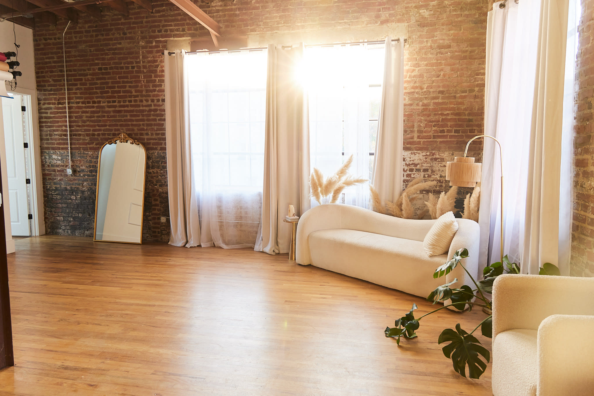 A cozy photoshoot setup features a vintage chair, a textured armchair, and large windows with sheer curtains allowing natural light to flood the space.