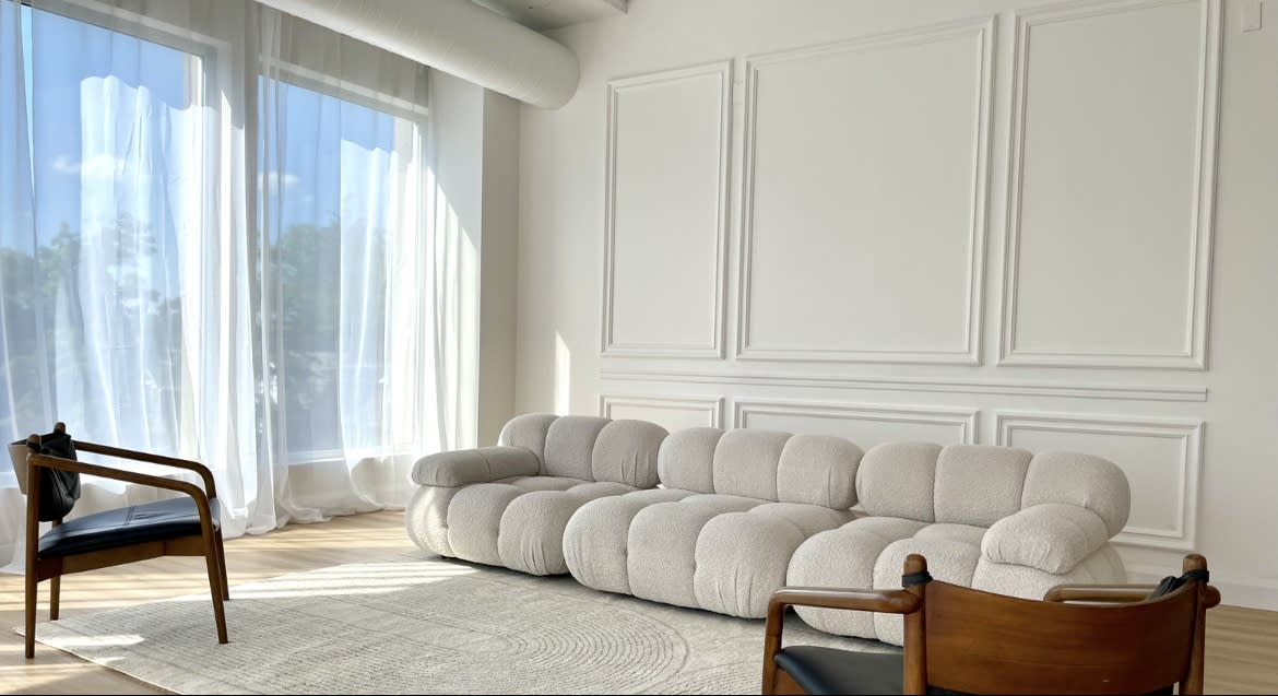 A photographer captures images of a subject posed on a soft, light-colored couch in a well-lit studio.