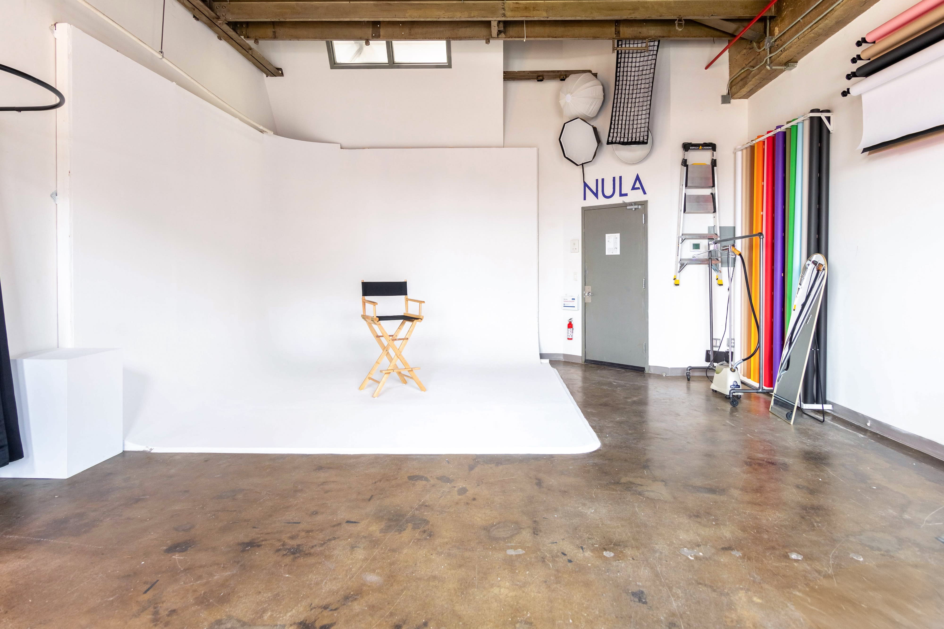 A photographer sets up equipment on a cart while a stylist looks on in a brightly colored studio during a photoshoot.
