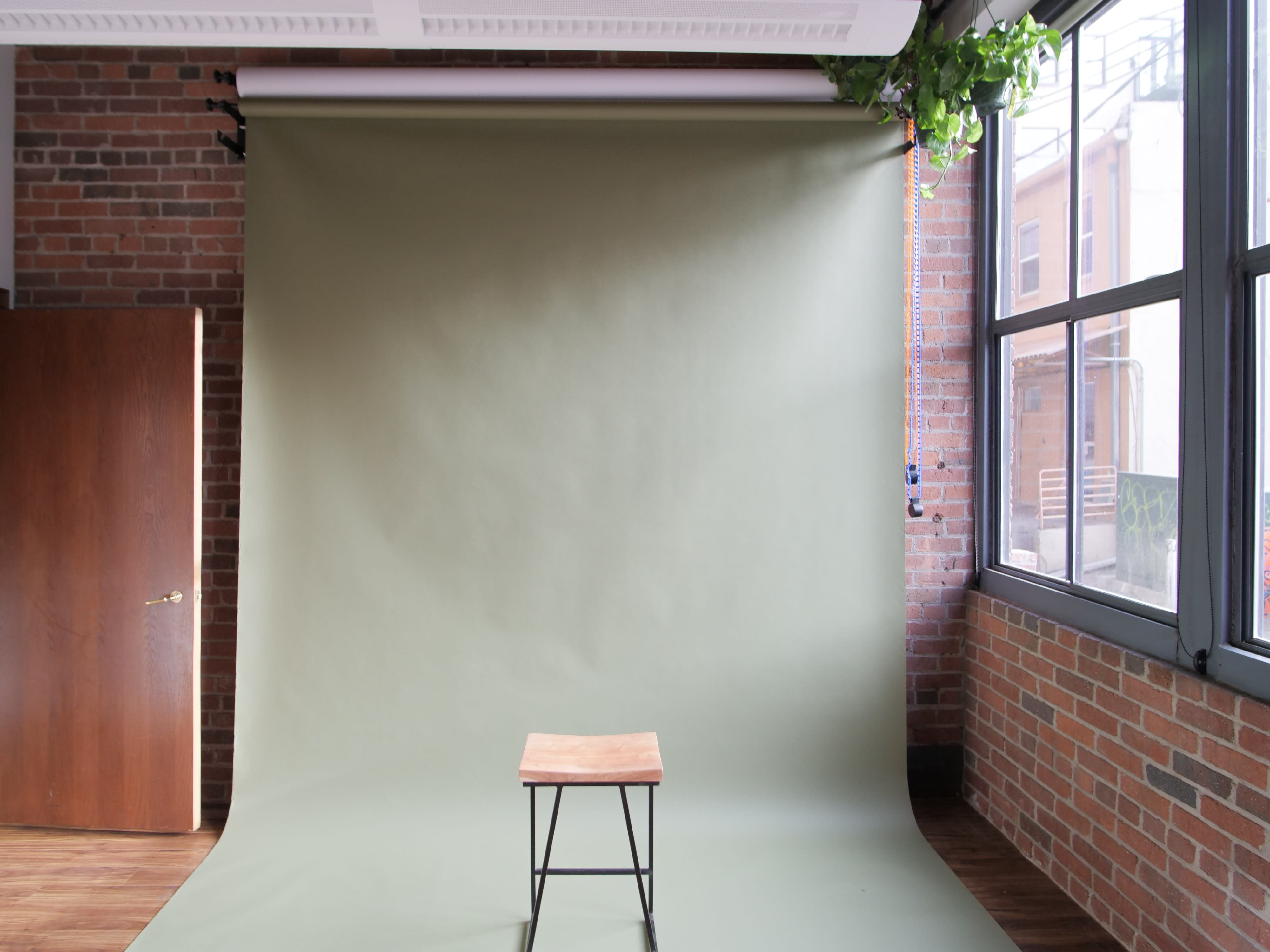 A woman sits on a stool, inspecting a camera in a photo shoot studio with a black backdrop.