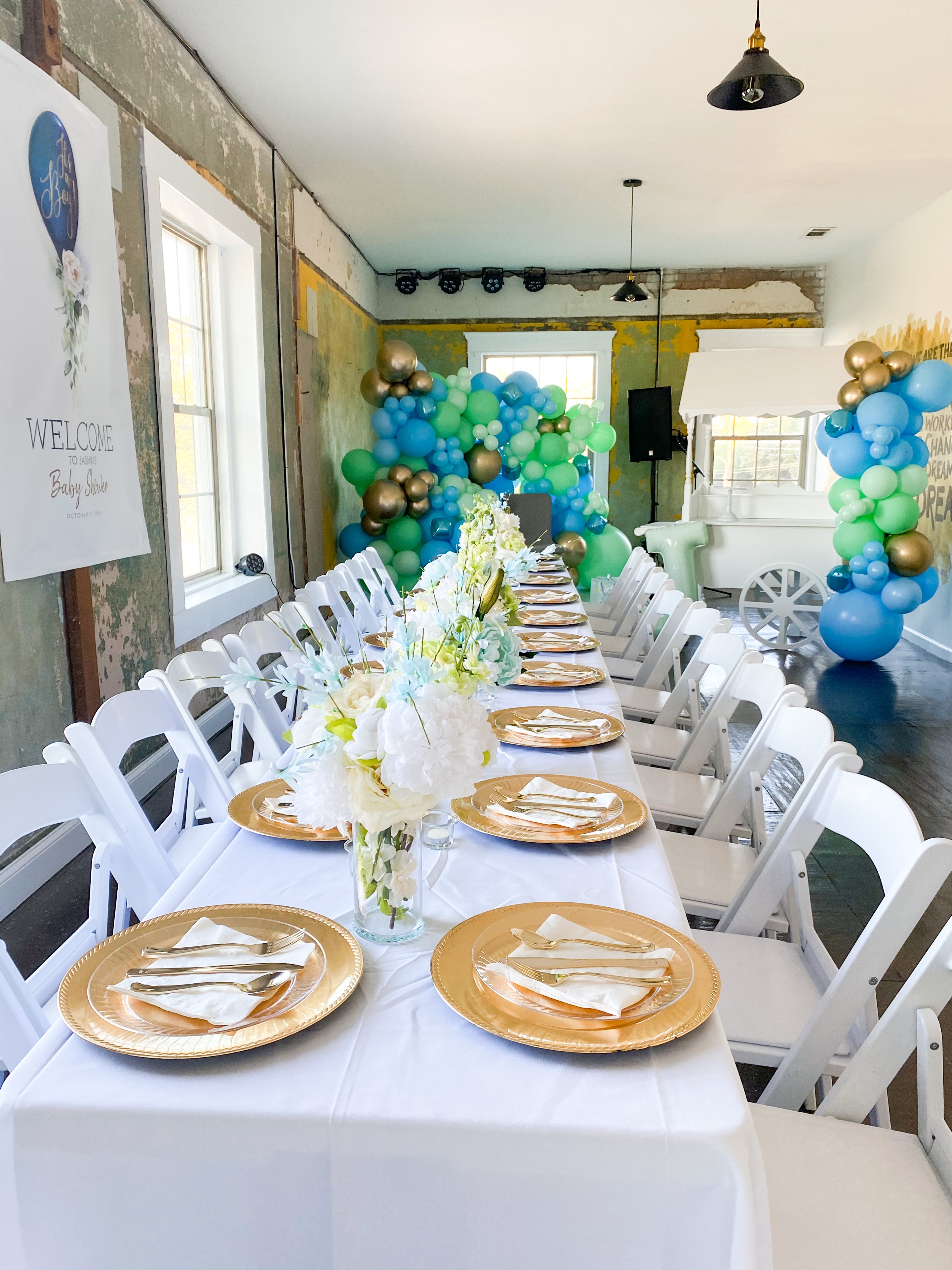 The scene features a decorated backdrop with a cluster of balloons in shades of pink and gray, alongside floral arrangements, set up for a bridal shower celebration.