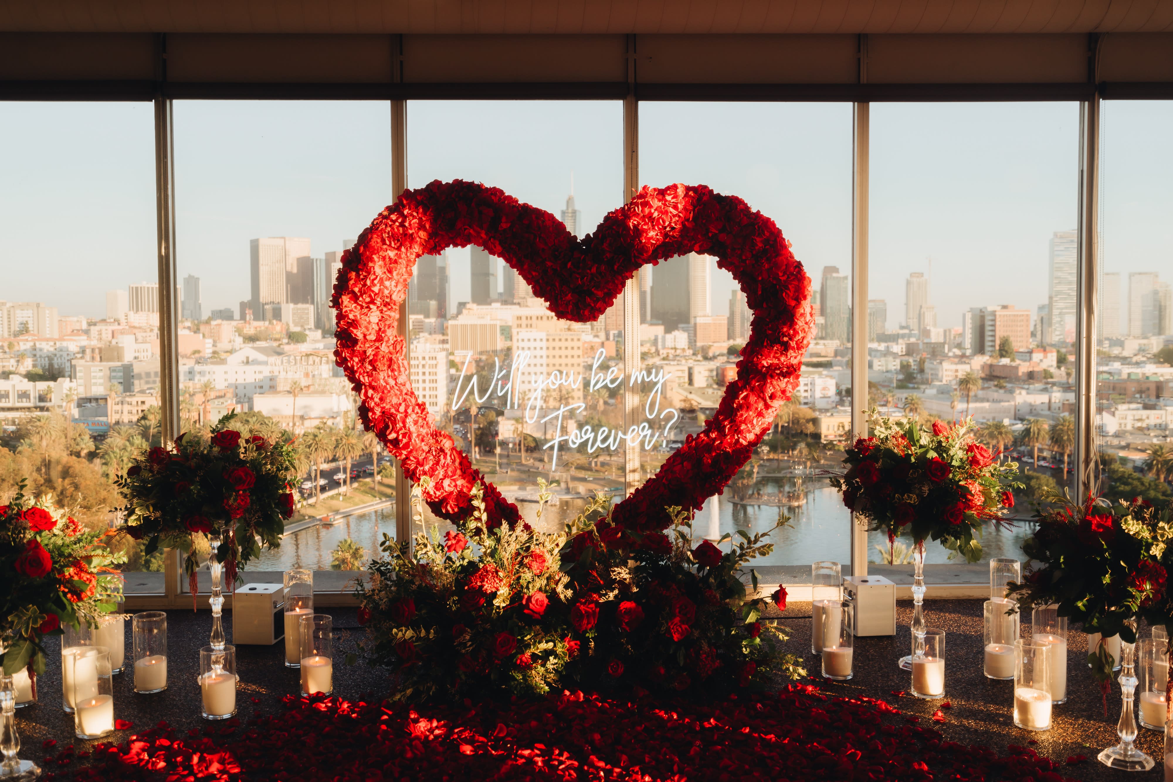 A person is proposing against the backdrop of a sunset visible through a modern, patterned window.
