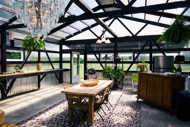 A long dining table is elegantly set with candles, seasonal decorations, and place settings in a greenhouse for a wedding reception.