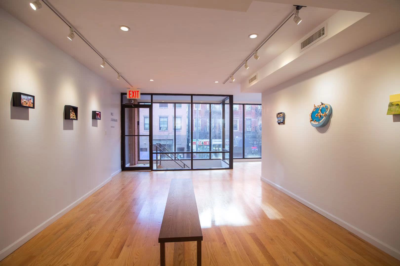 A wooden bench sits in front of vibrant paintings displayed on the walls of an art exhibit.