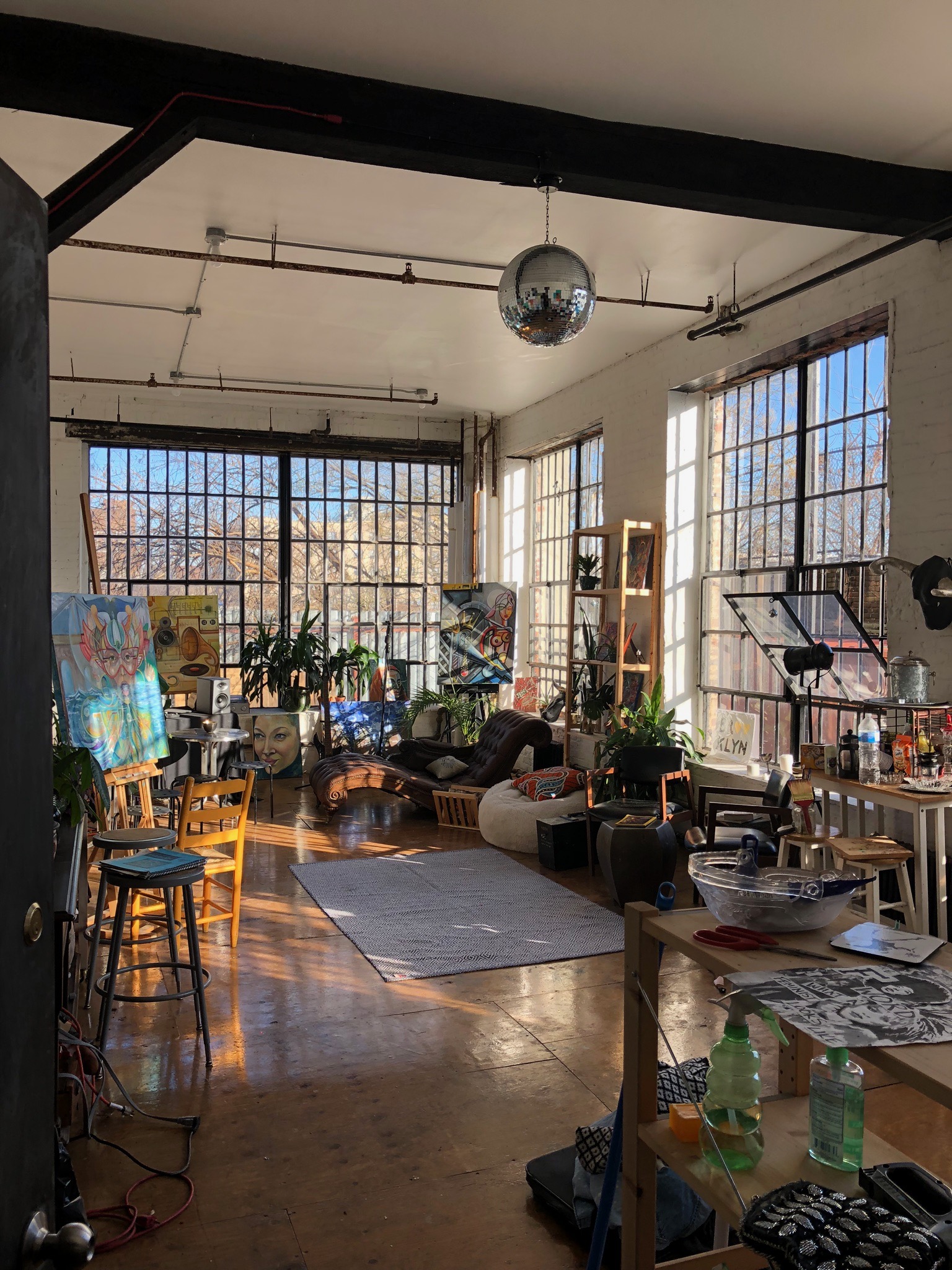 A model poses on a red stool in a sunlit room with large windows and artistic decor.