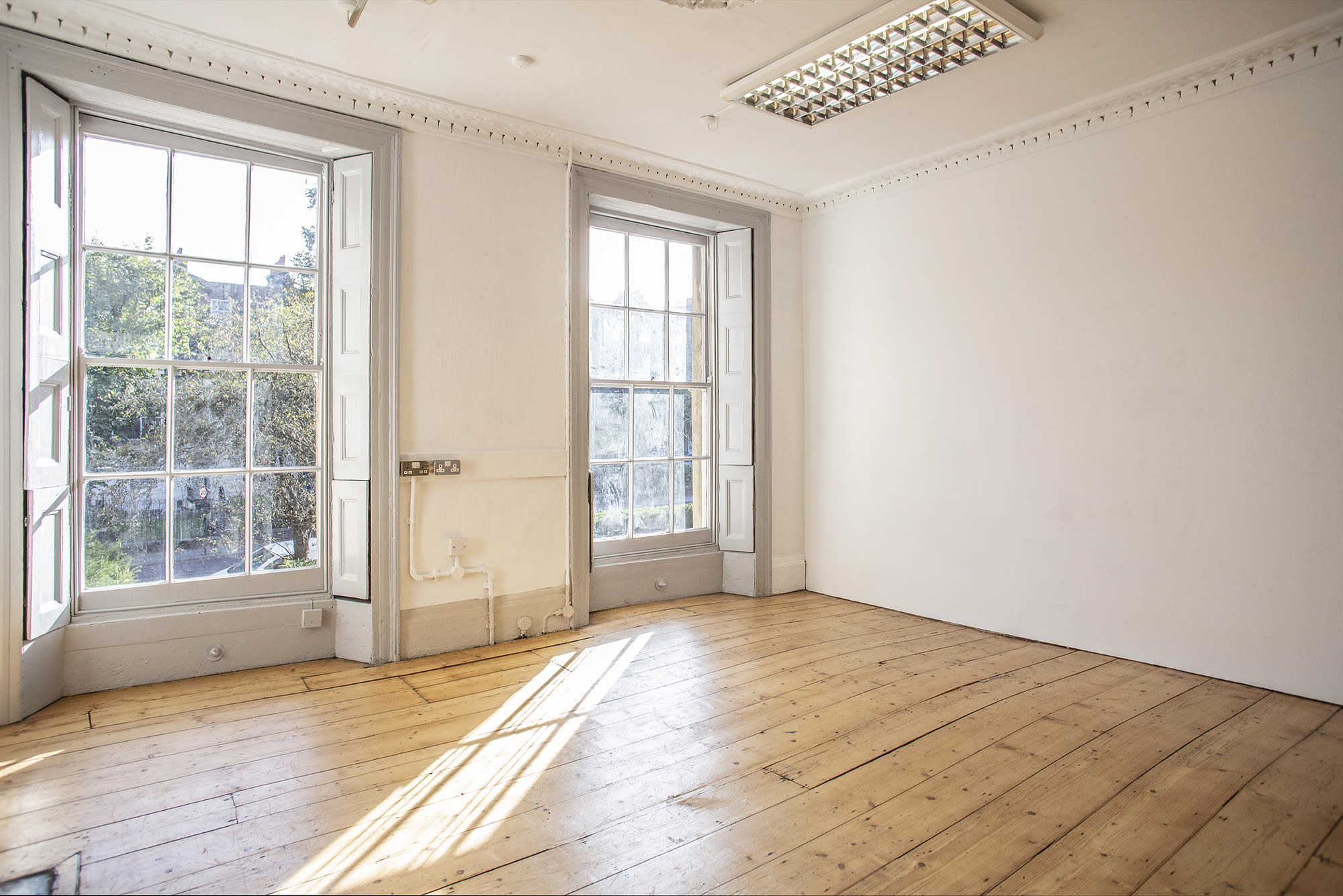 The image shows a photo studio setup with a large softbox light, a camera on a tripod, and a wooden chair placed on a patterned rug.