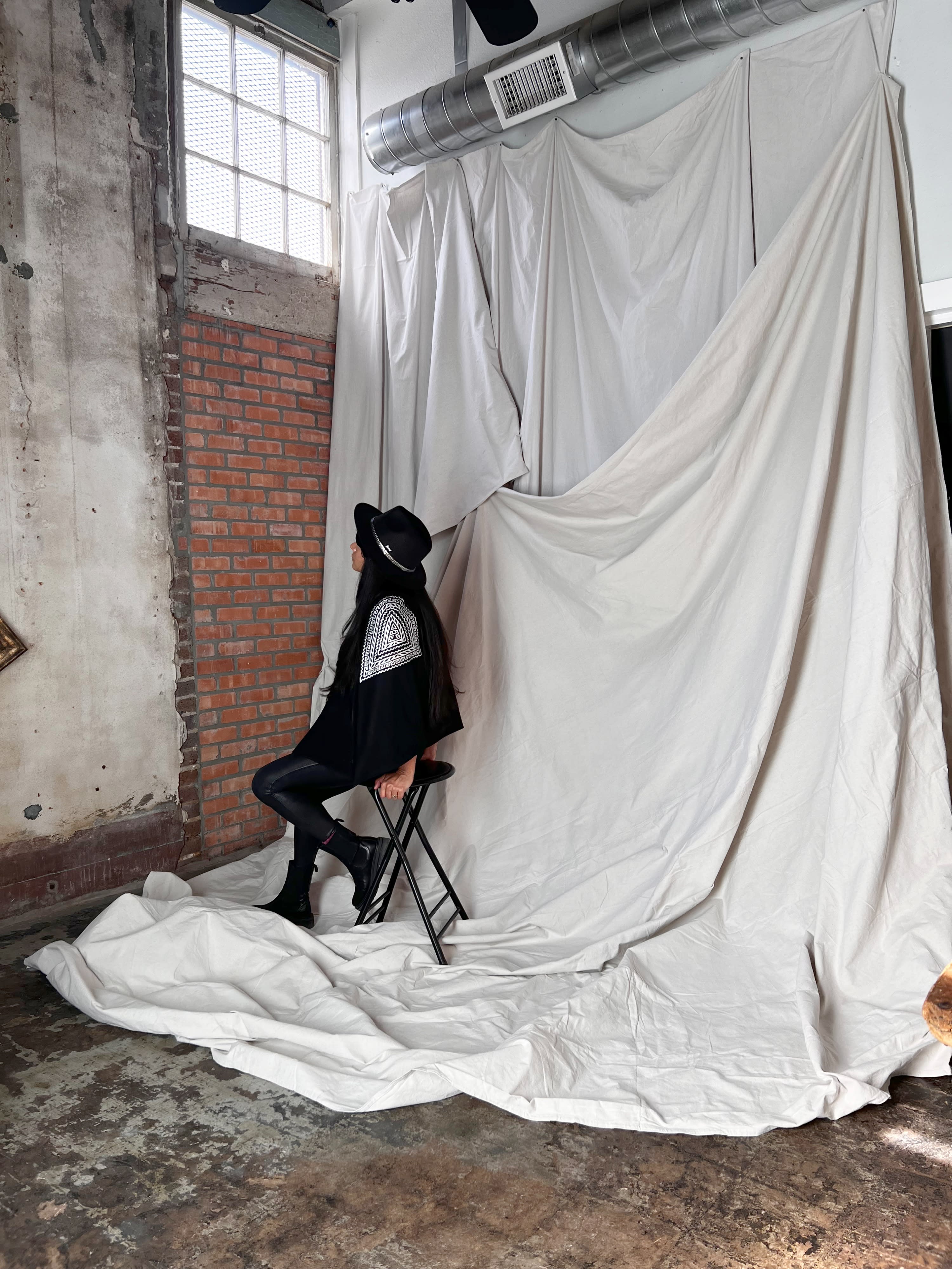 A woman sits blindfolded and bound to a chair, while a man sits behind her, also restrained, in a dimly lit warehouse setting.