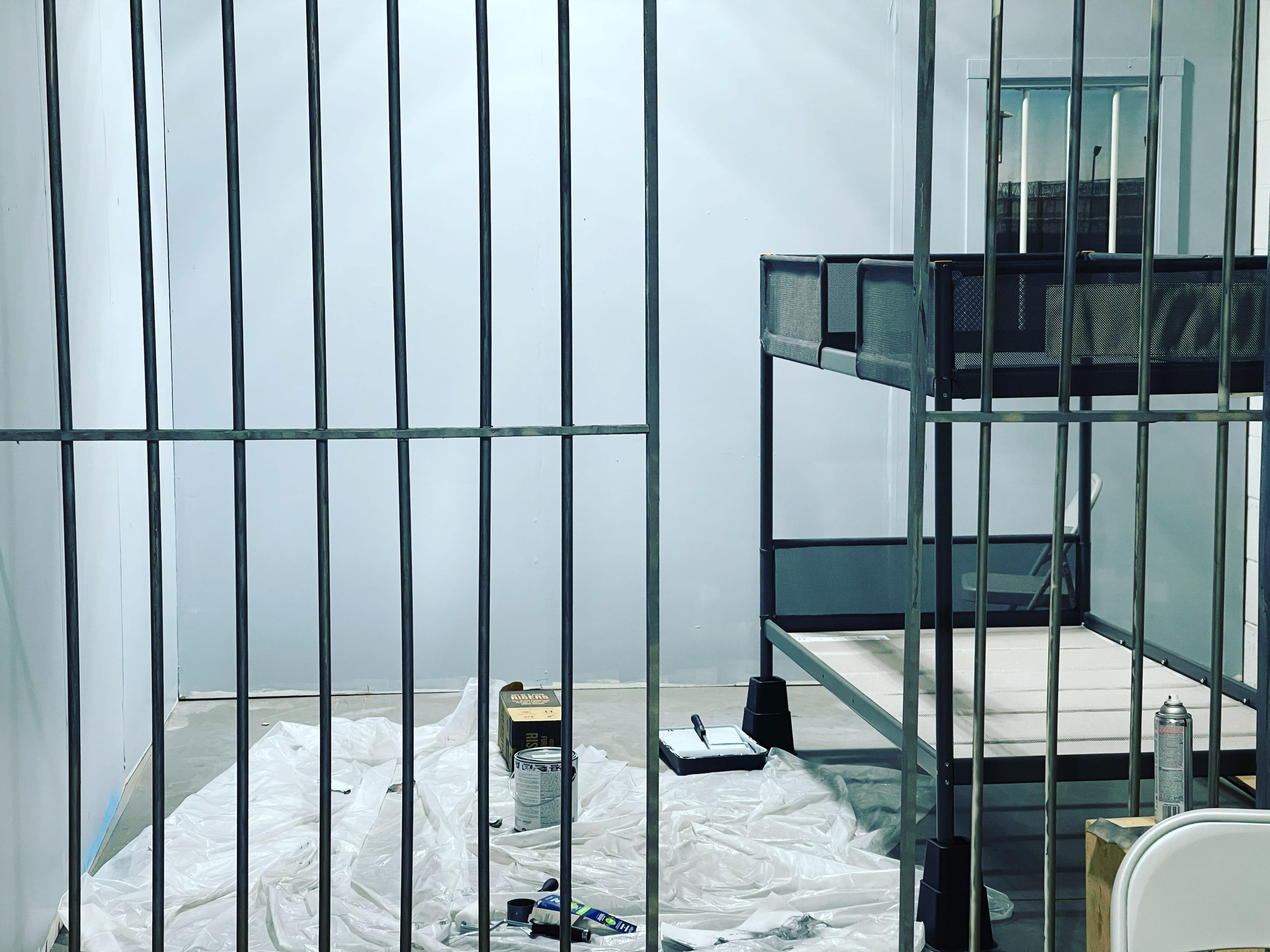 A model in an orange outfit poses behind metal bars, creating a dramatic scene.