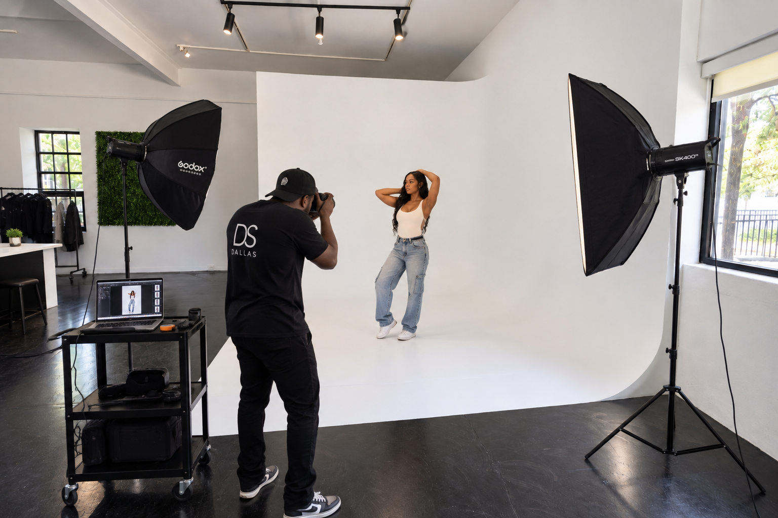 A model poses in a stylish chair surrounded by potted plants during a product photo shoot.