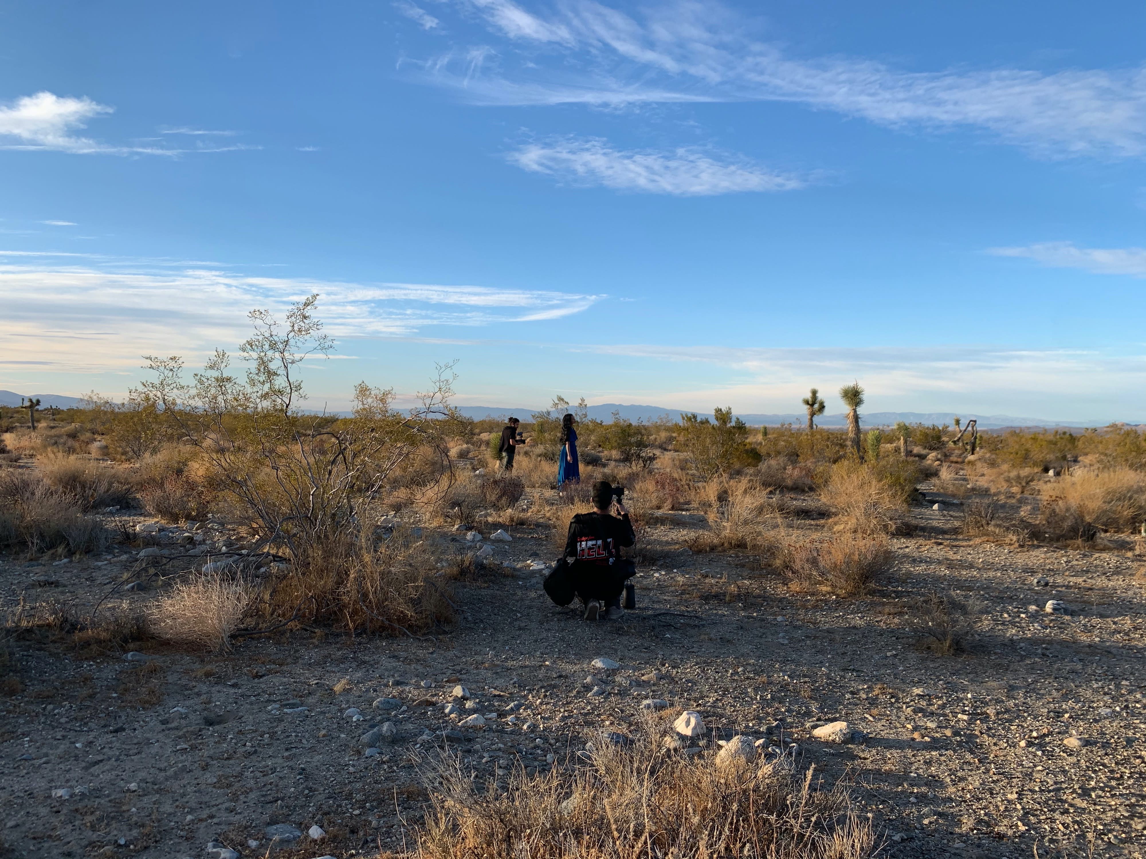 A film crew sets up lights and cameras for a night shoot in a desert area, with one crew member on a ladder overseeing the scene.