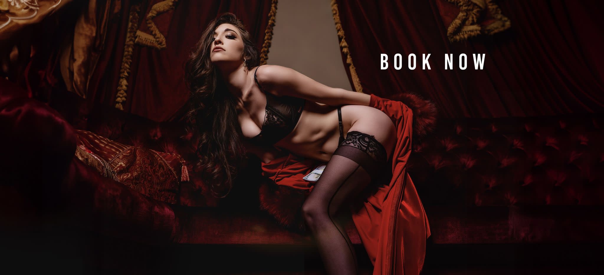 A model poses confidently in a dimly lit studio, holding a whip and wearing a stylish lingerie outfit.