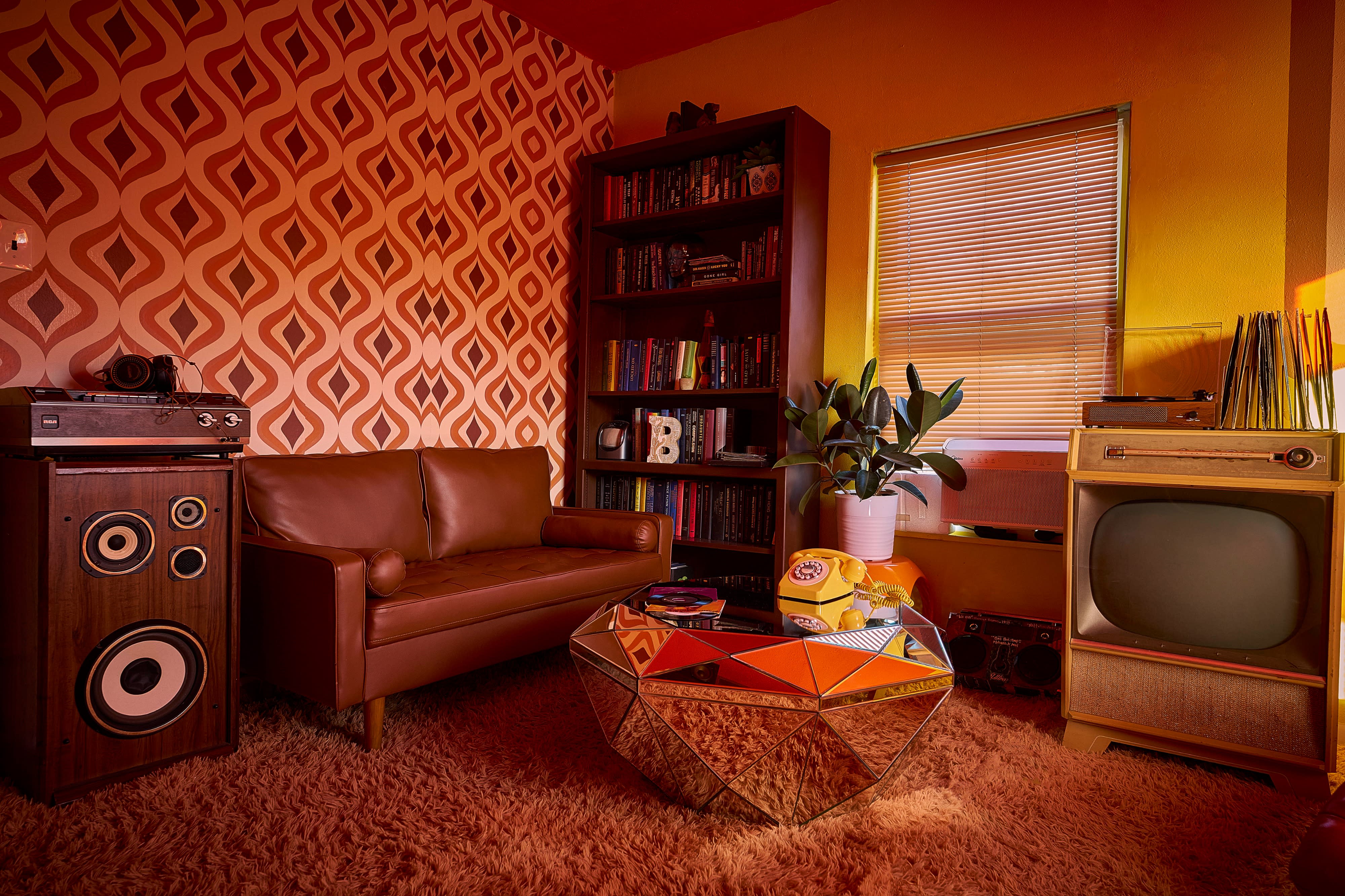 A person poses confidently next to a large array of vintage speakers while holding a drink in a vibrant setting.