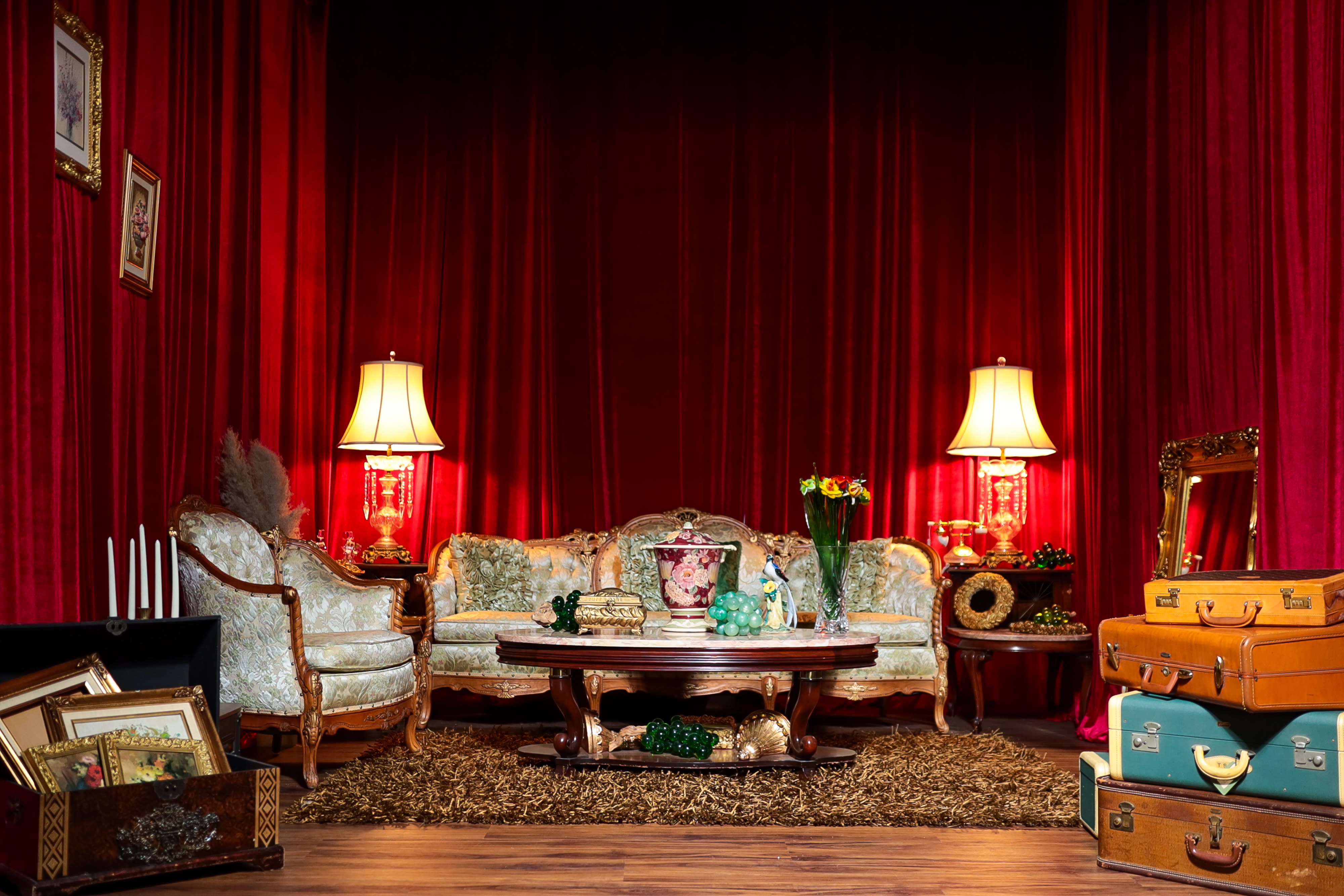A model poses on a coffee table in a lavishly decorated living room, wearing stylish sunglasses and a corset while showcasing a glamorous look.