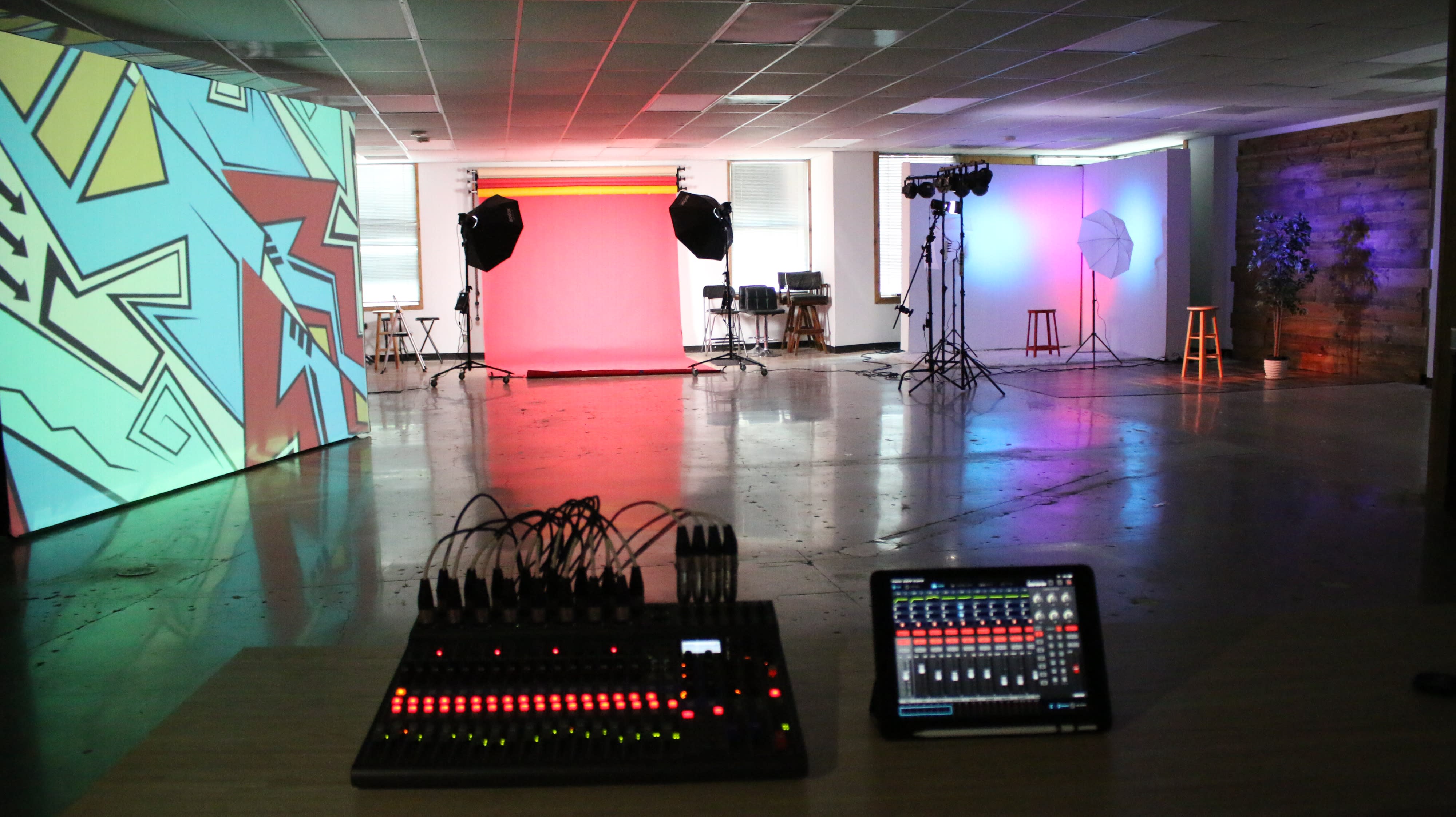 A performer stands at a microphone in front of a red backdrop during a video shoot.