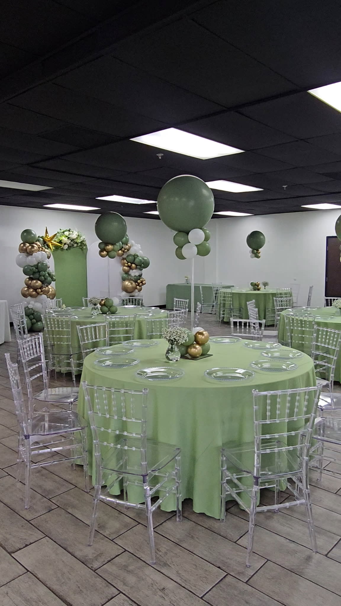 The scene shows a beautifully arranged baby shower setup with a round table adorned with plates and decorations, surrounded by pastel balloons and floral displays in a themed area.