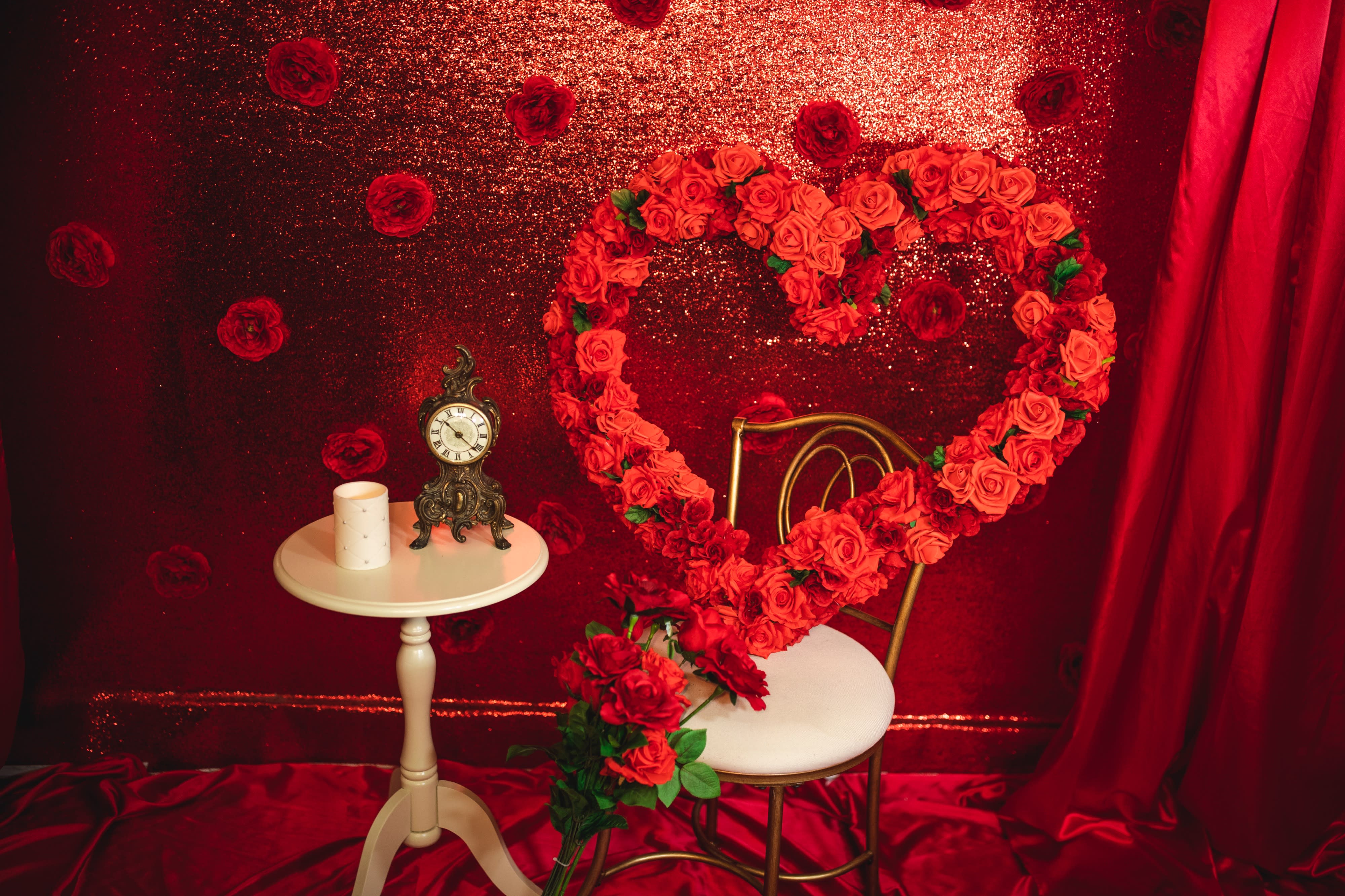 A woman poses for a video shoot while sitting on a pink chair against a floral green backdrop with a neon sign that says "Hello gorgeous."
