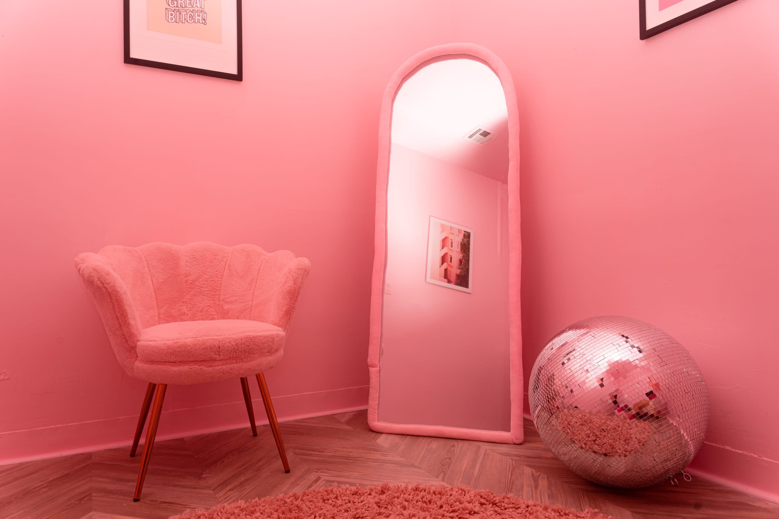 A woman in a pink satin robe sits on a light-colored sofa in a pink-themed room with decorative elements.