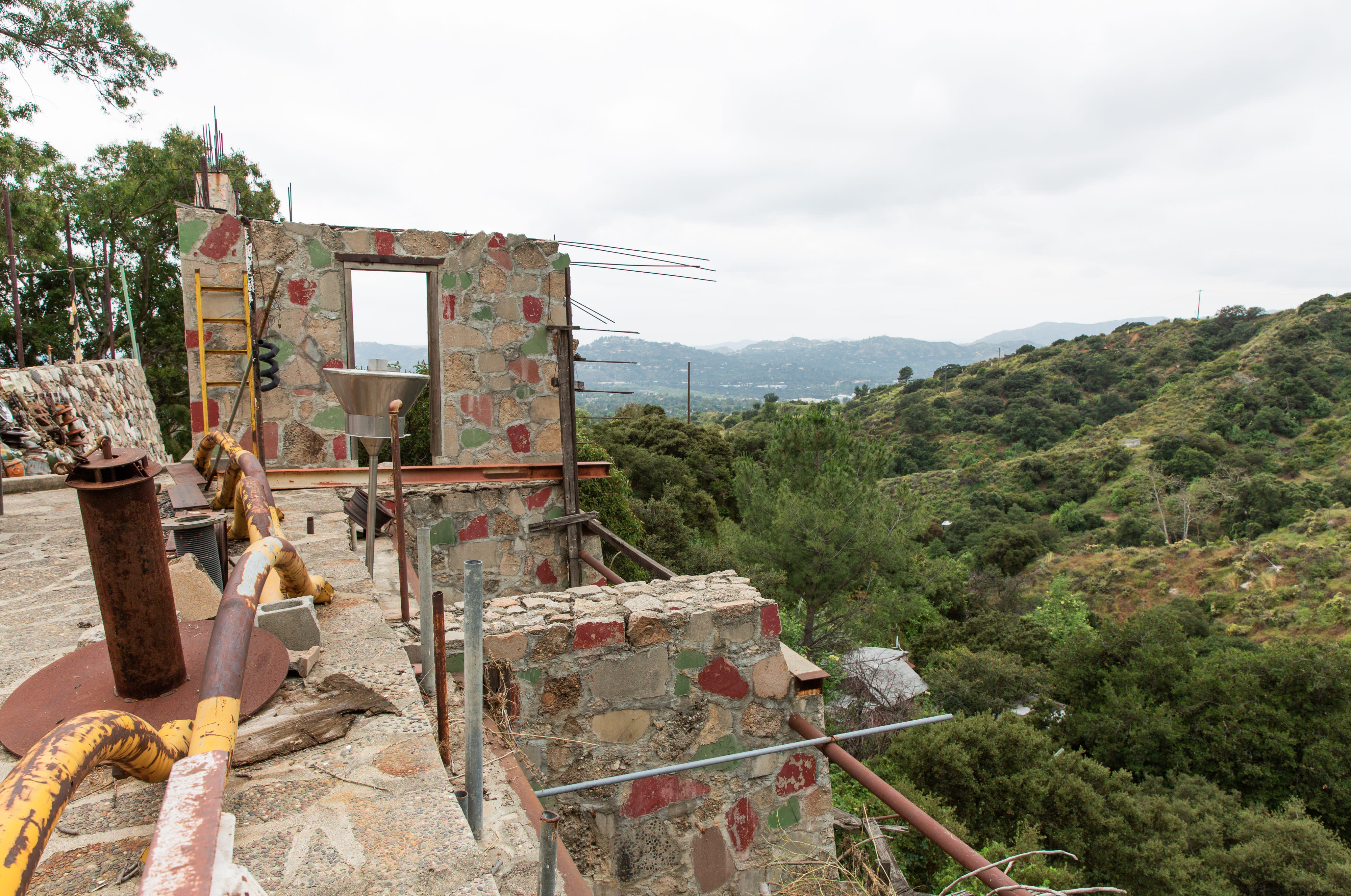 A person stands near a decorated trailer while preparing for a photoshoot in a rural setting surrounded by rolling hills and livestock.