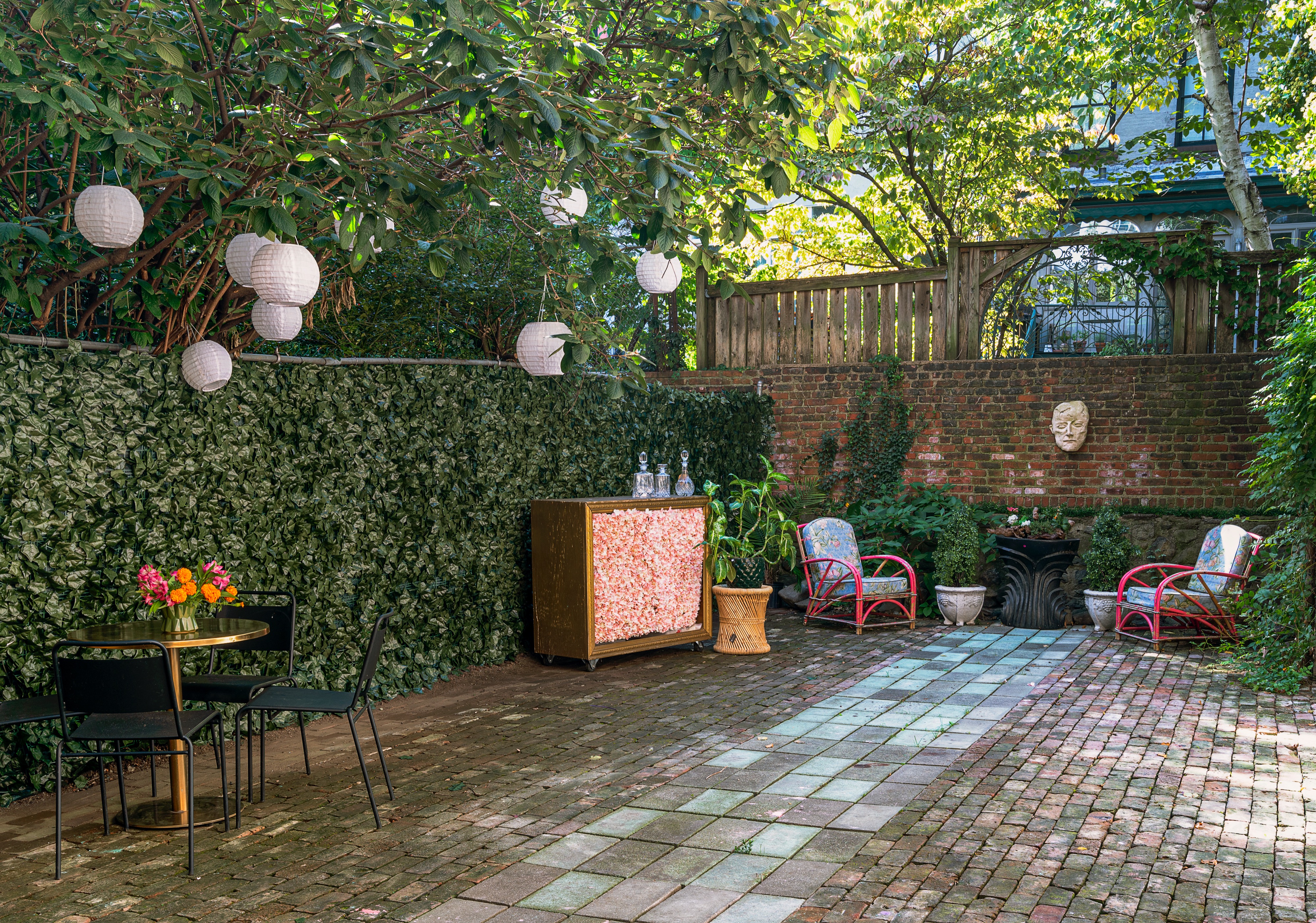 Four individuals sit around a table in a garden setting, engaged in an activity while surrounded by lighting equipment.