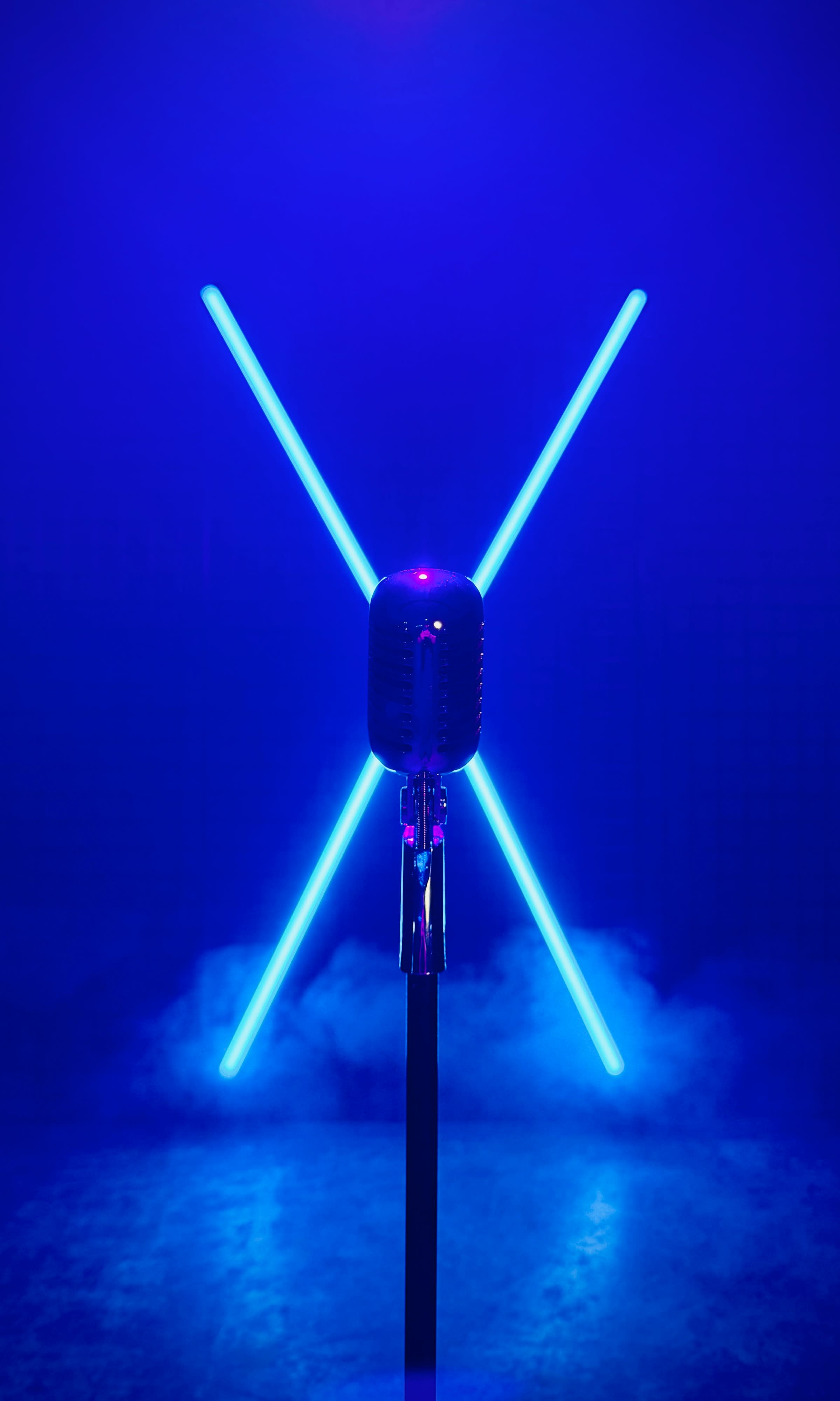 A performer sits on the ground amidst fog, illuminated by purple lights from a backdrop of circular lamps.