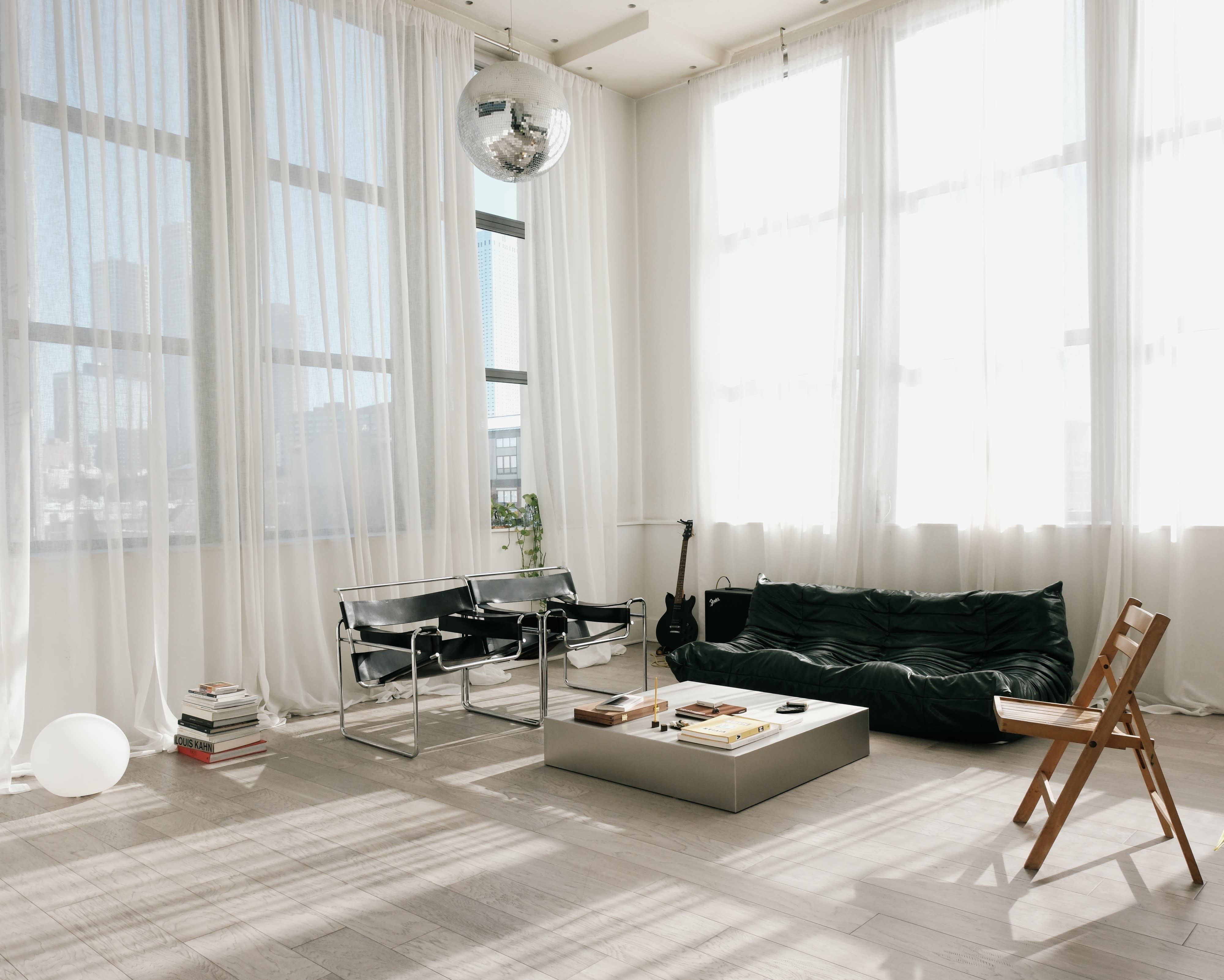 A minimalistic indoor space features two black chairs and a potted plant, with large windows allowing natural light and a view of the city outside.