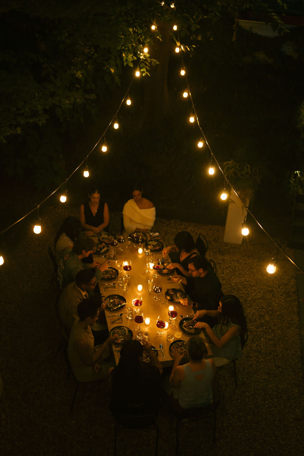 A beautifully arranged table displays an array of pizzas and salads, while guests in white attire mingle and celebrate during the engagement party.