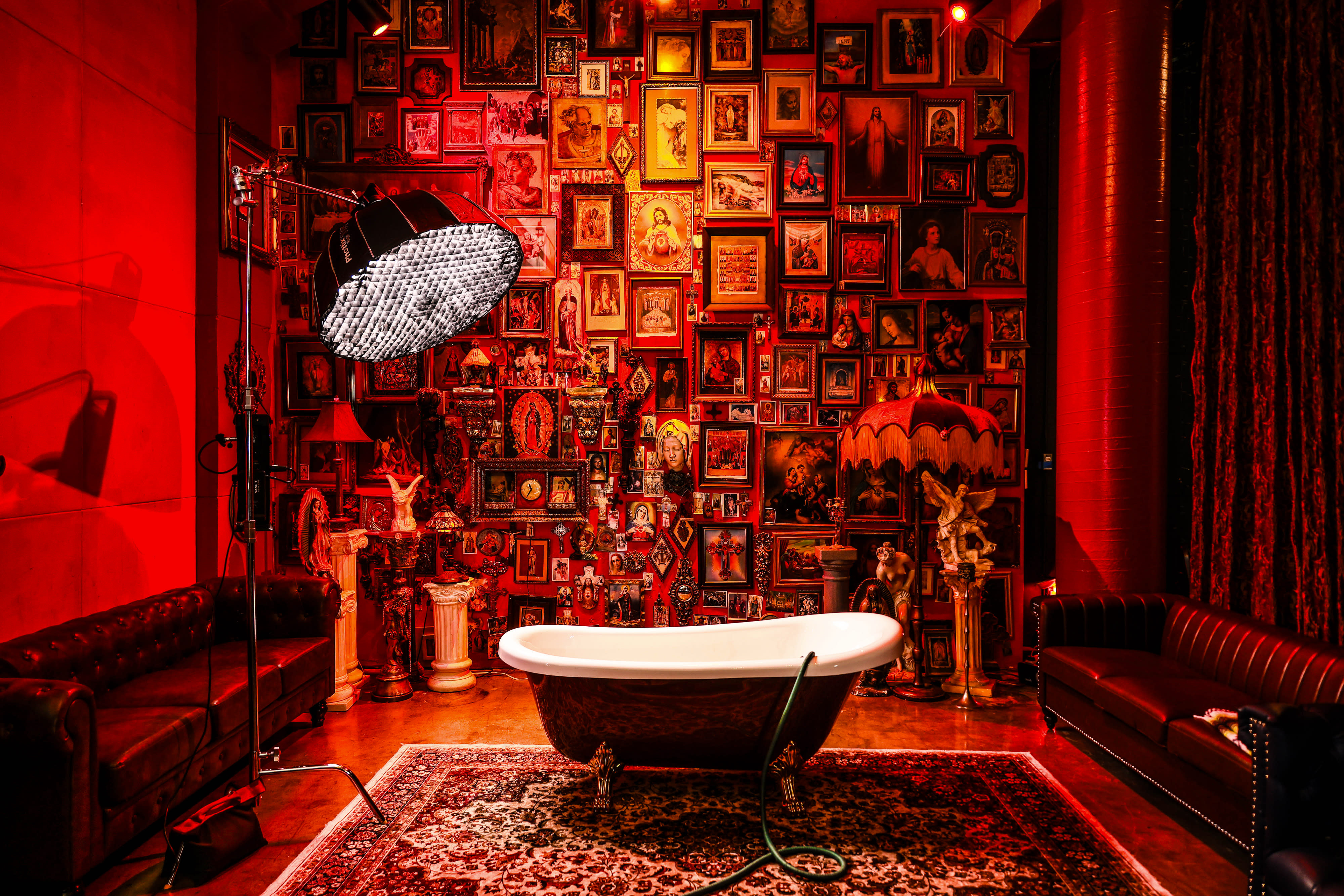 A model poses on a vintage couch in a room decorated with various framed images and a warm, colorful glow.