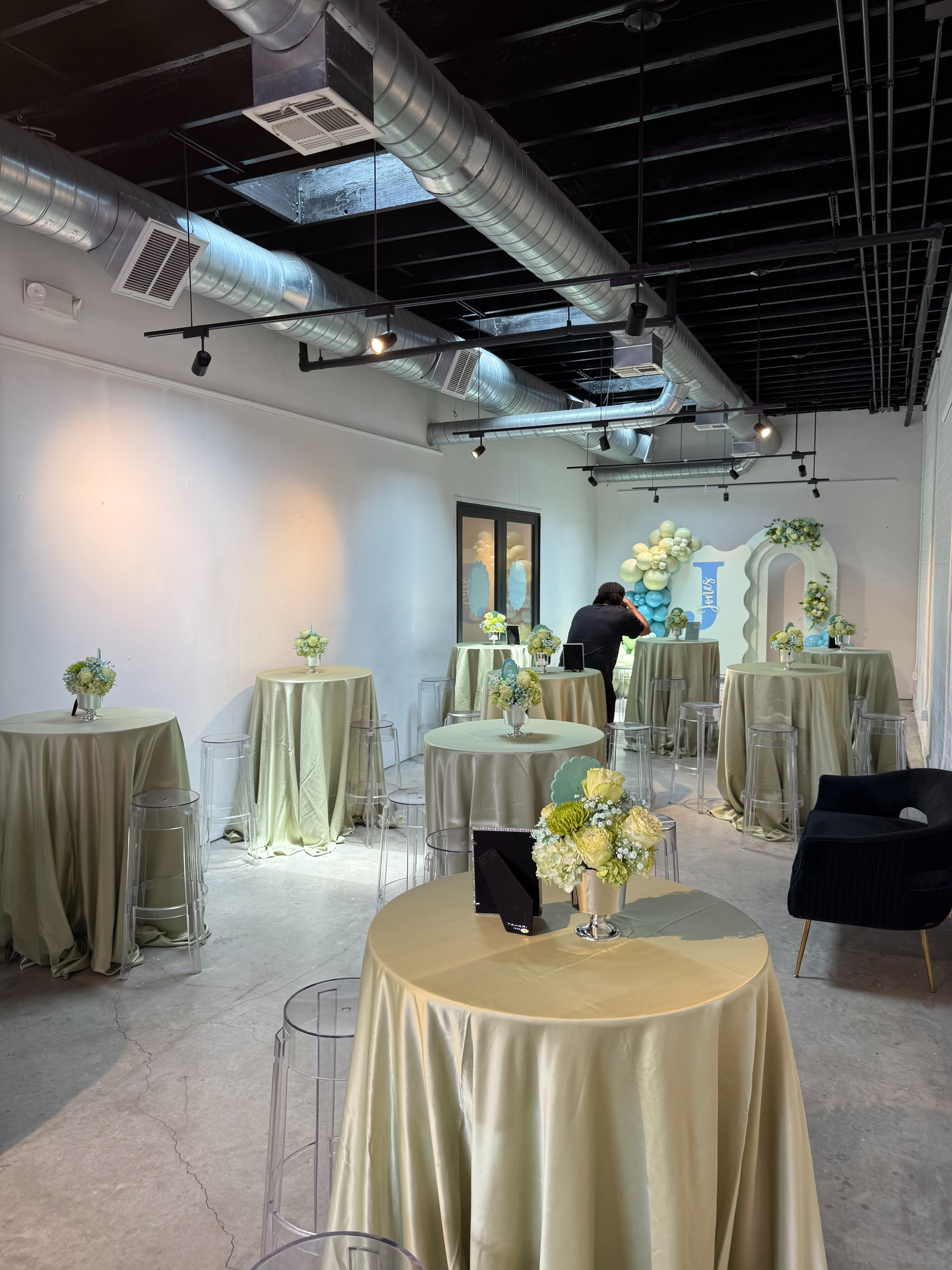 A DJ party setup is underway in a spacious venue with guests mingling around high-top tables.