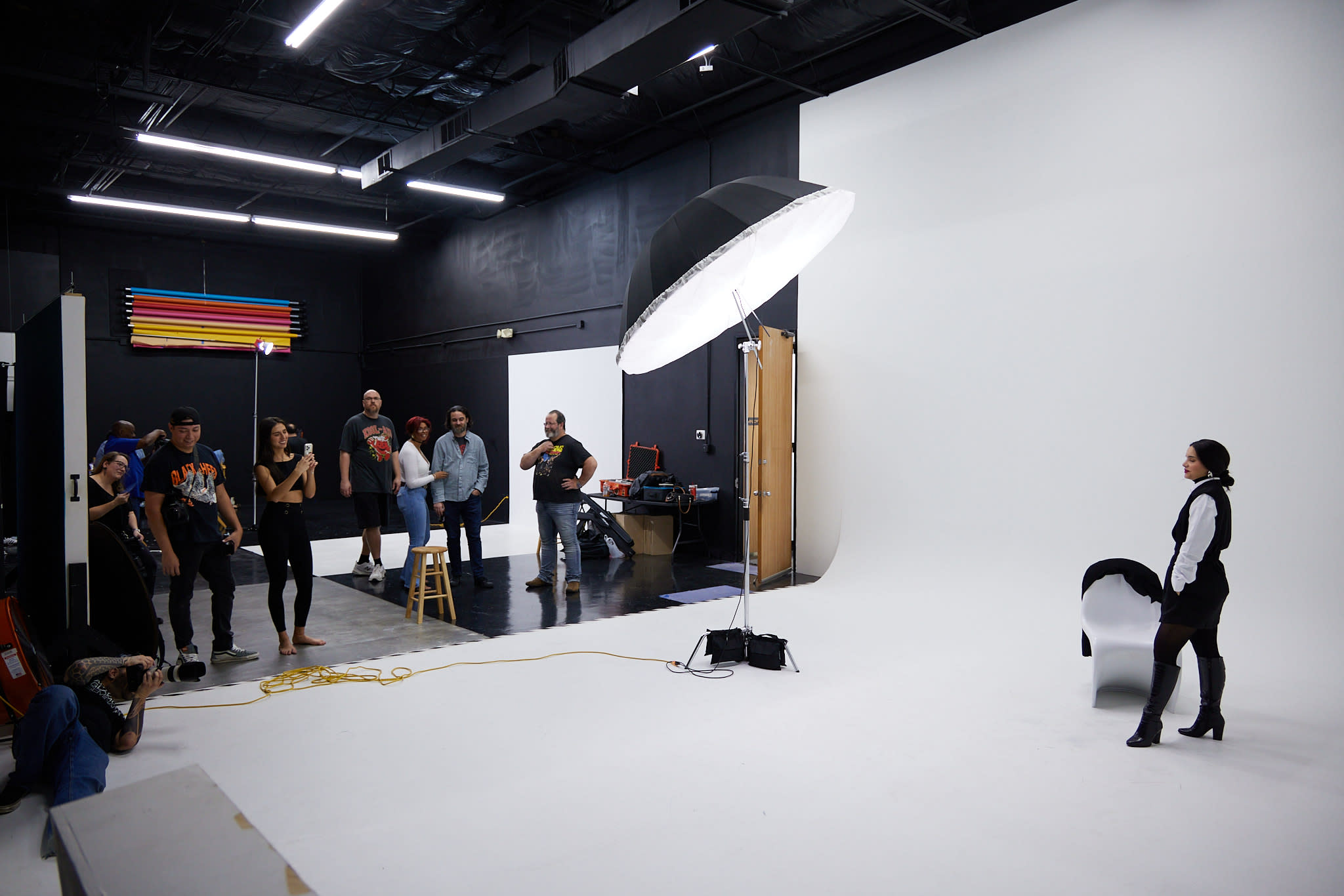 A photographer captures a group of five women posing in front of a vibrant red backdrop during a photoshoot.