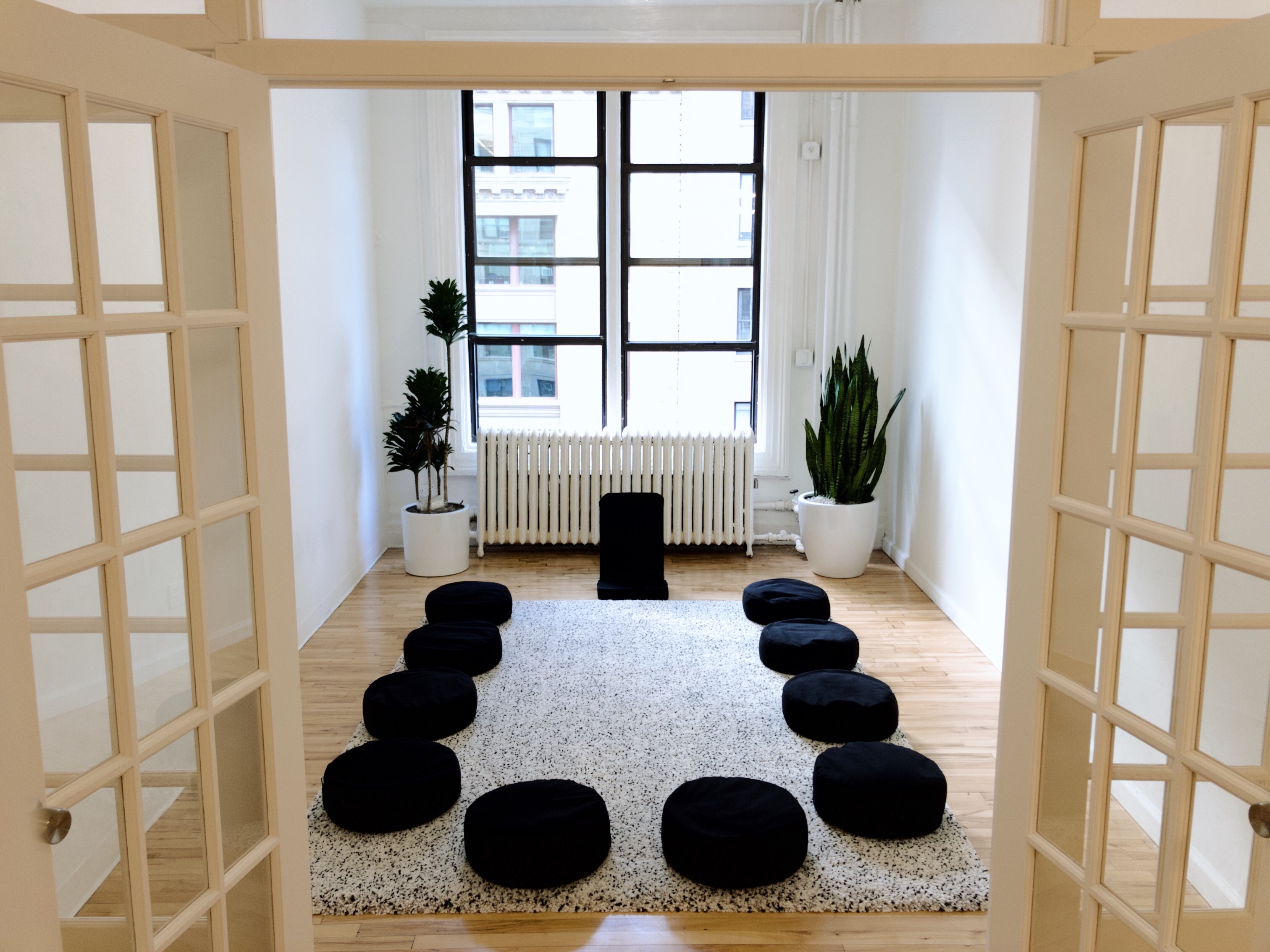 A group of individuals are seated on yoga mats, practicing meditation under soft lighting with fairy lights in the background.