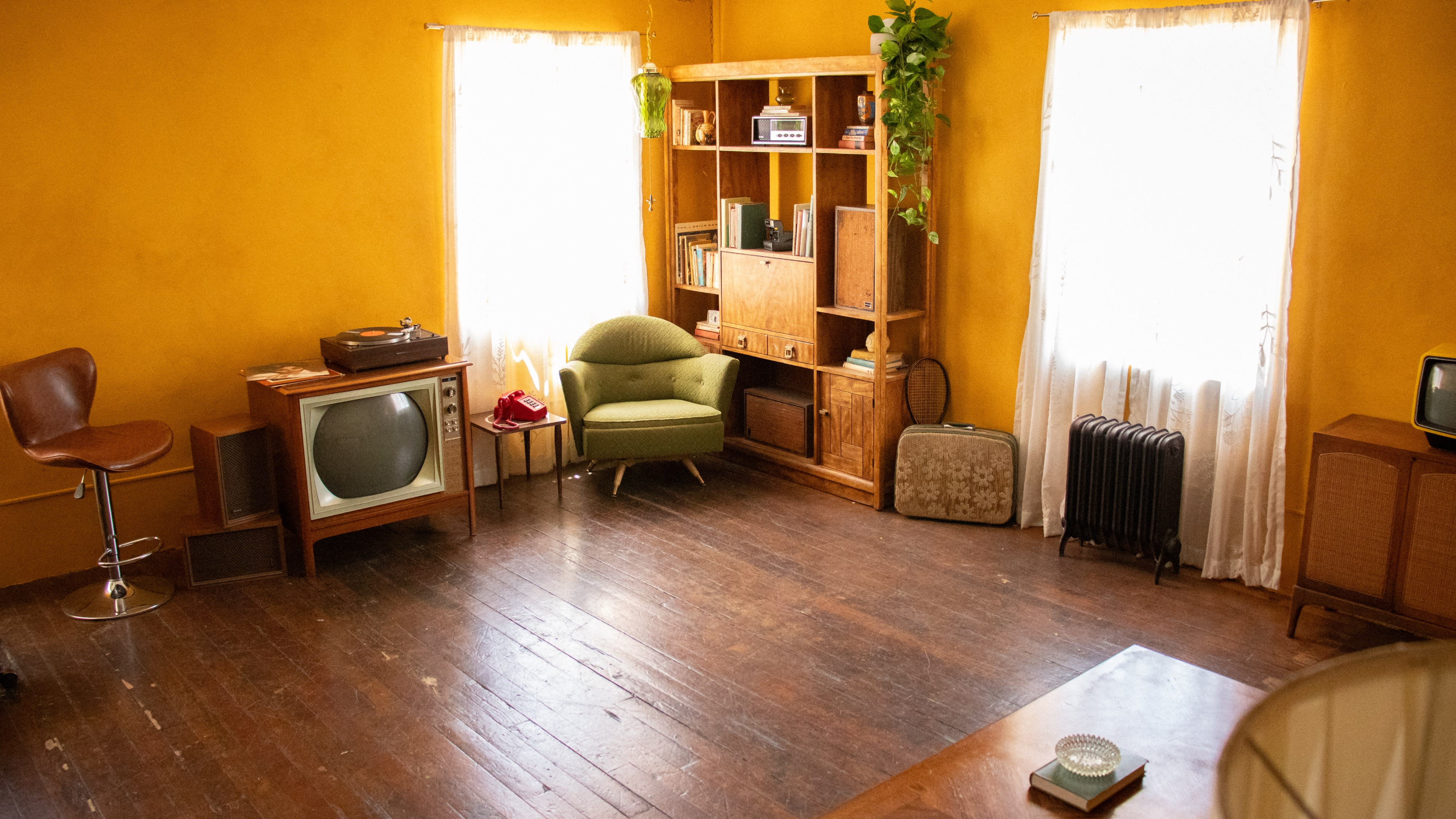 A model poses sitting on the carpet in a vintage-style room surrounded by mid-century furniture.