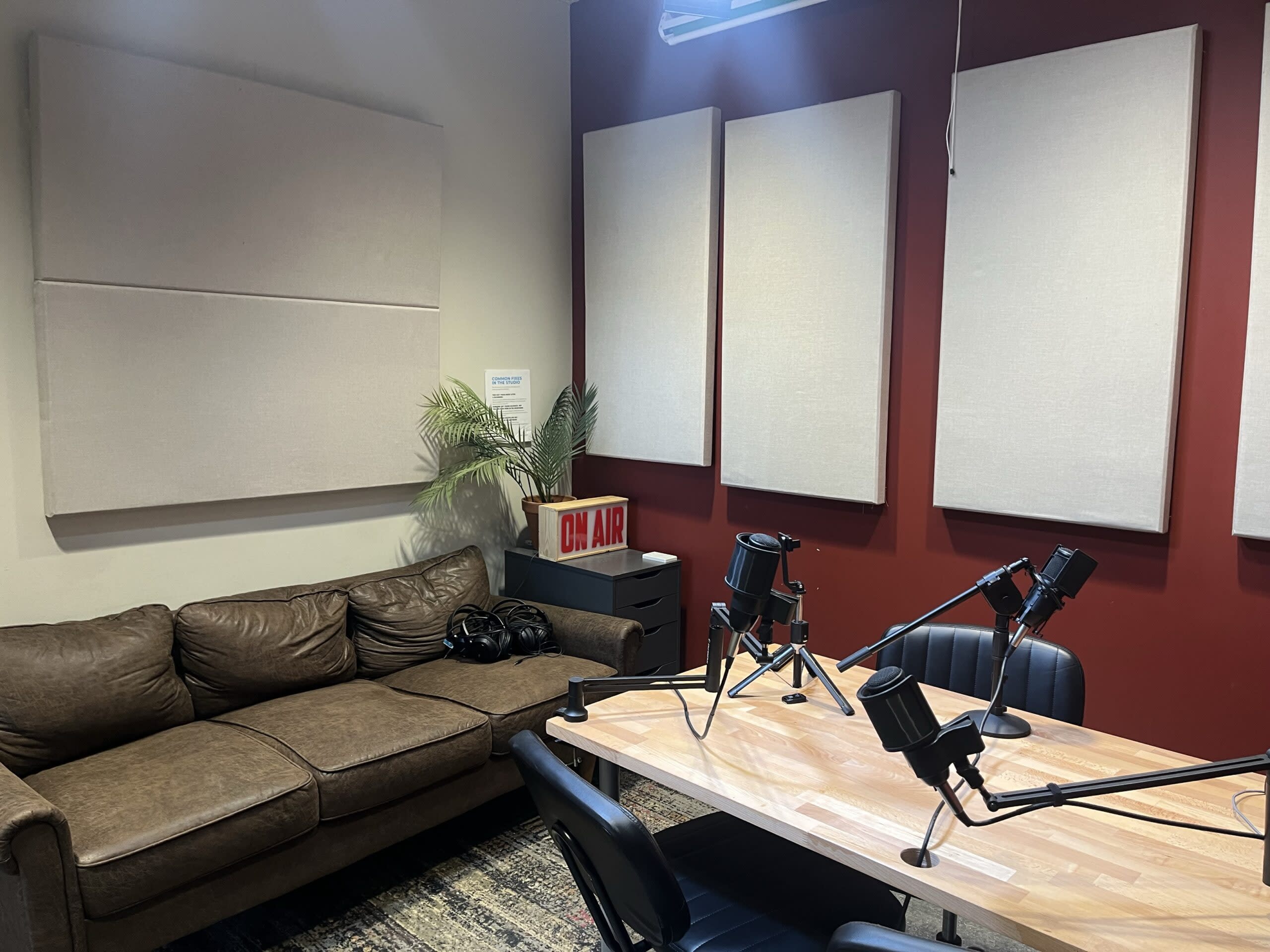 Two microphones on adjustable stands are positioned near orange chairs, with a wooden sign reading "ON AIR" indicating a recording setup.