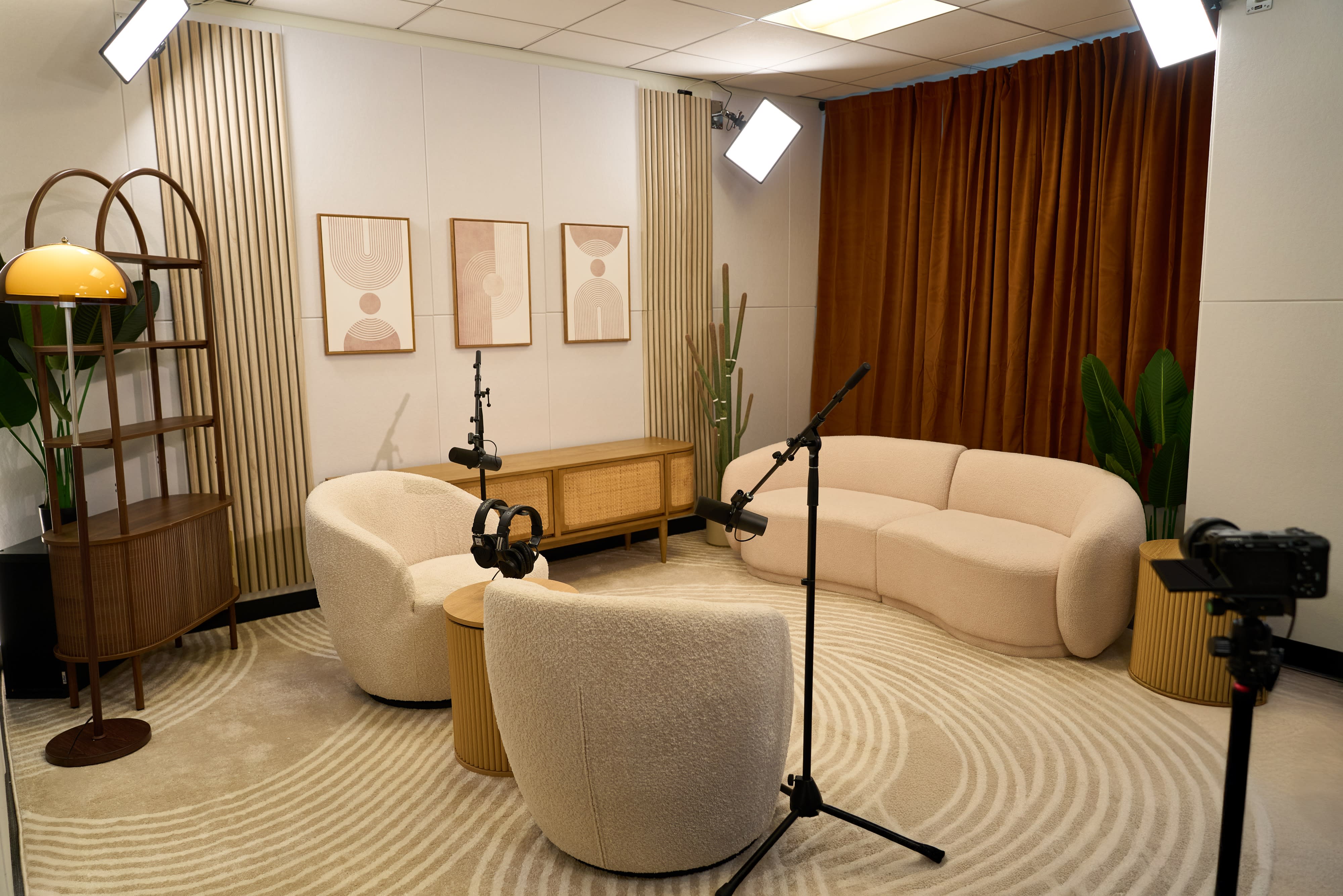 Two hosts sit in a brightly decorated studio, laughing and engaging in conversation while preparing to record a podcast.