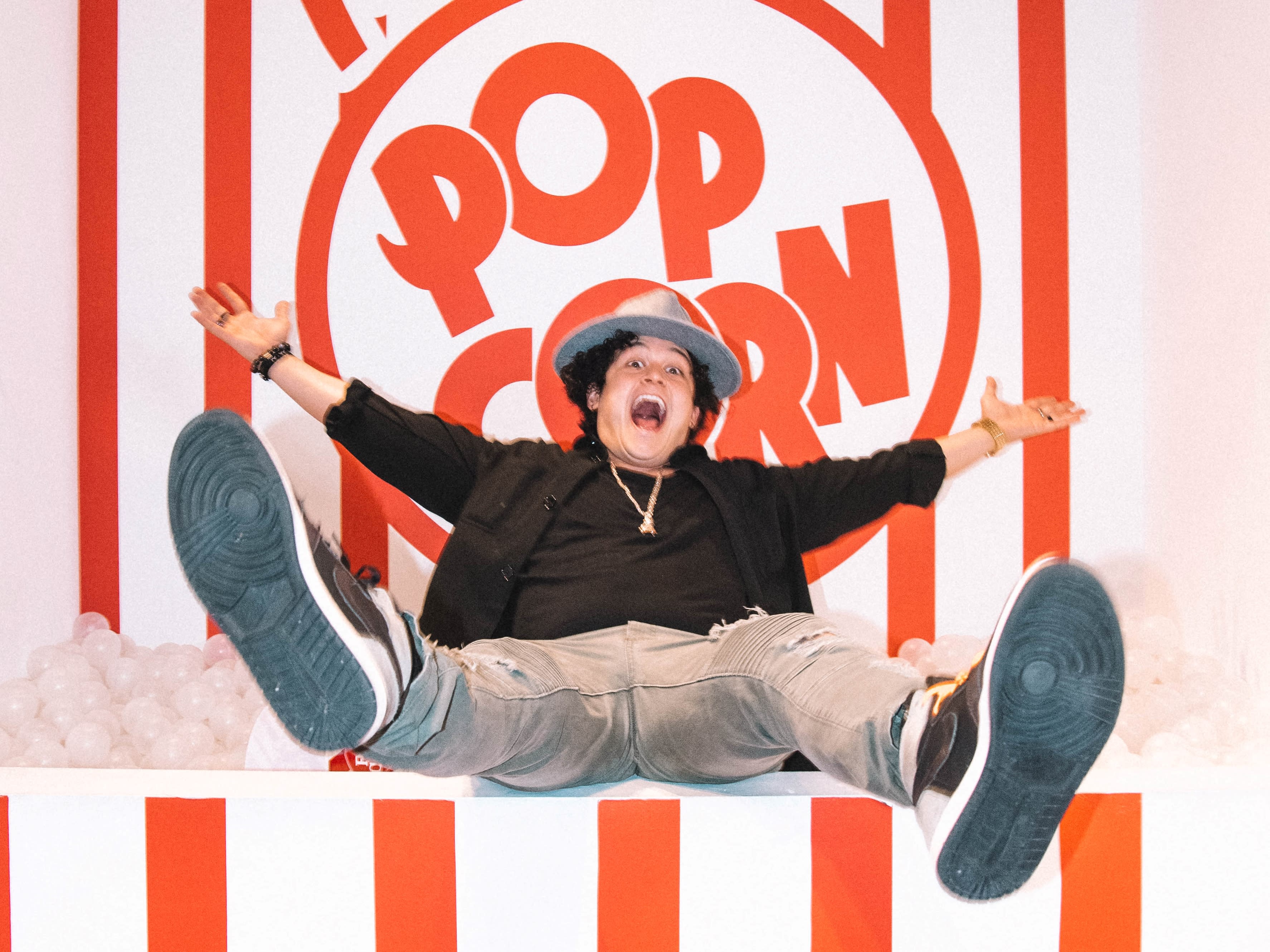A man sits on a bench with two children, one on the left and one on the right, in front of a pink wall featuring the neon sign "Out of your league."