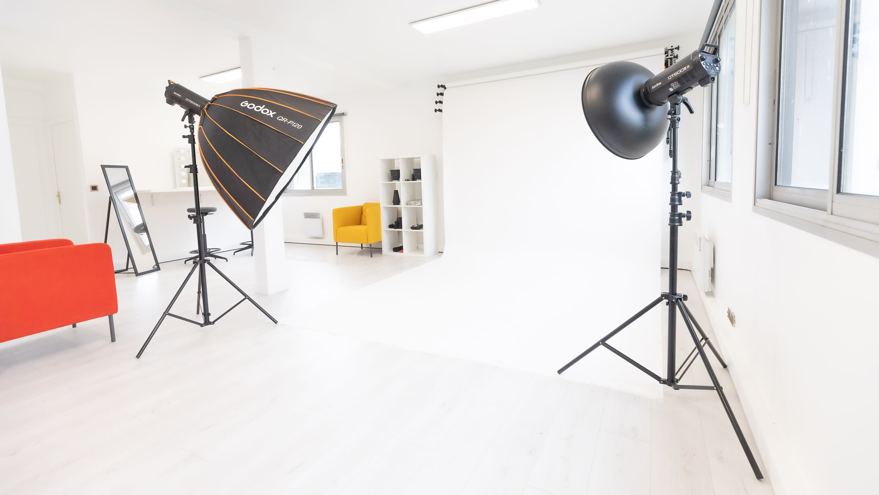 A model dressed in a sheer, textured gown is being adjusted by two stylists in a studio setting for a fashion shoot.