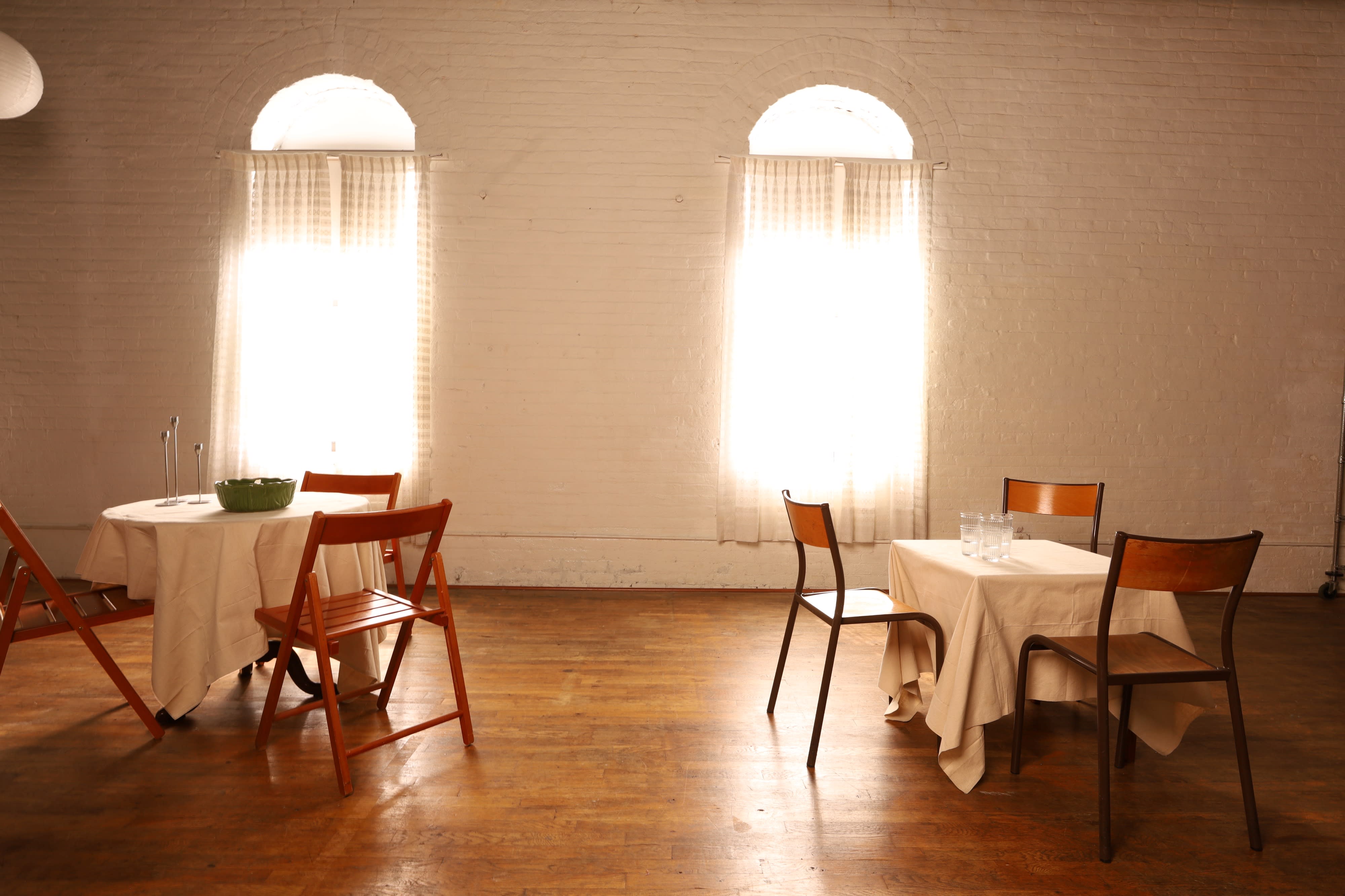 A group of five people gathers around a long dining table adorned with candles and food for a birthday celebration in a rustic indoor setting.