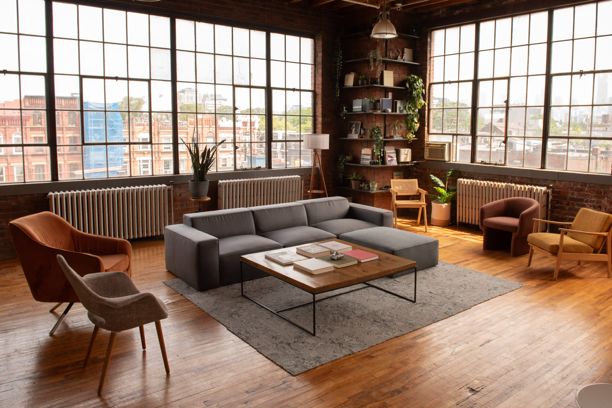 A bright, spacious loft features large windows, showcasing urban views, with a cozy seating arrangement and decorative plants.