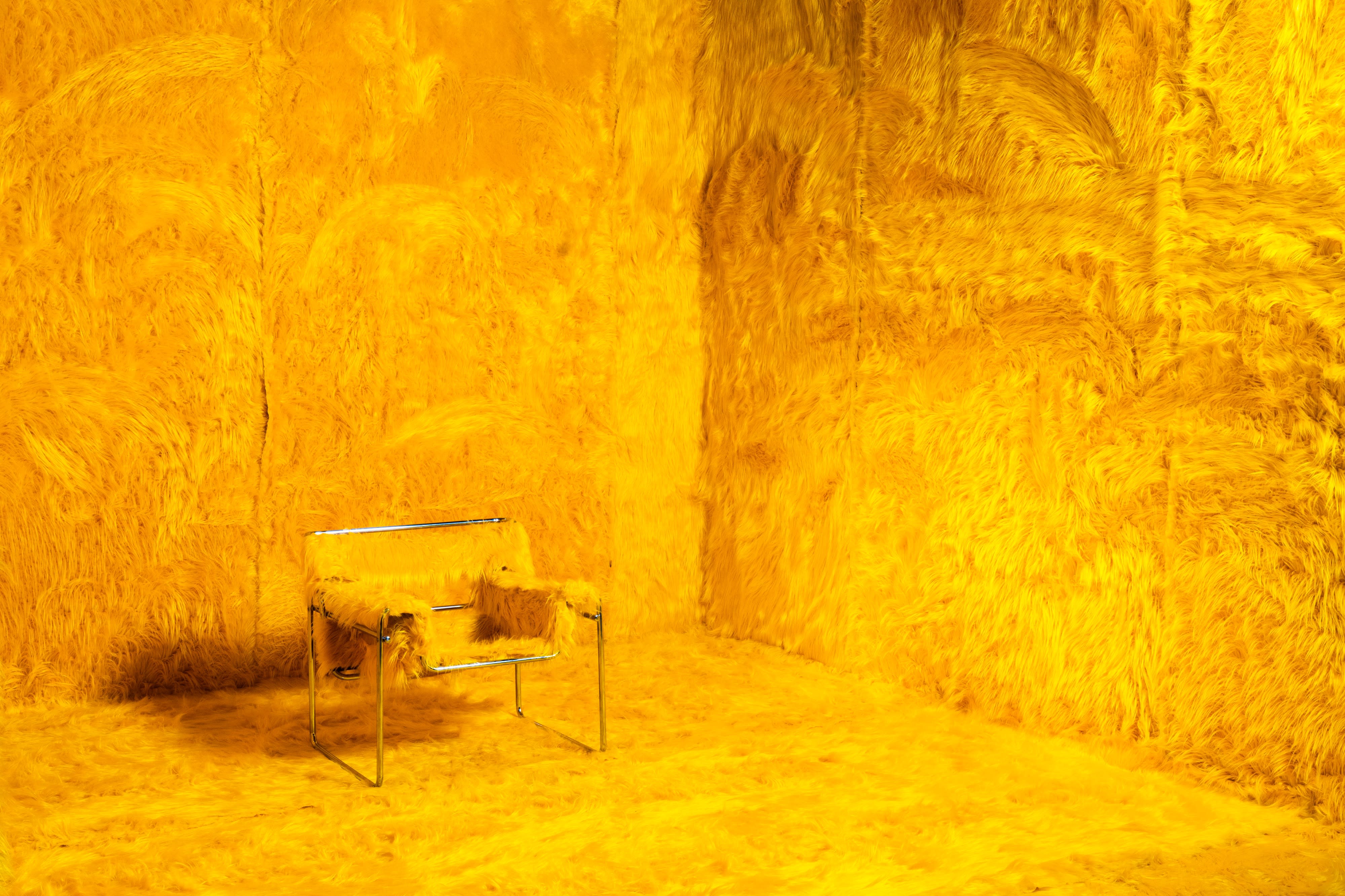 A musician poses with an electric guitar against a bright yellow furry backdrop during a video shoot.