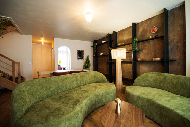 A person sits on a green cushion in a music video setting, illuminated by a spotlight, while looking at their phone.