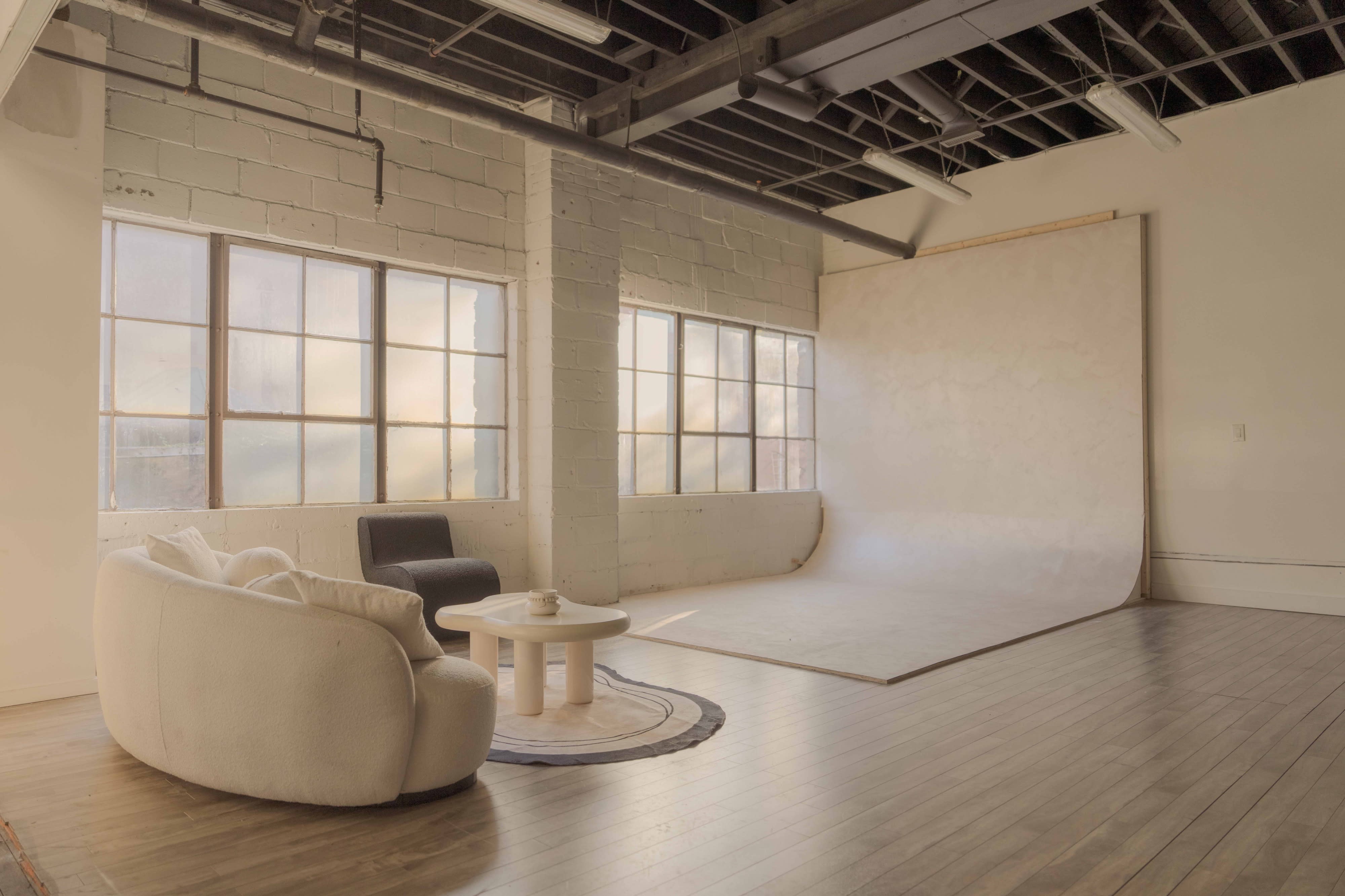 A photography studio features a large curved backdrop with natural light streaming in through the windows.