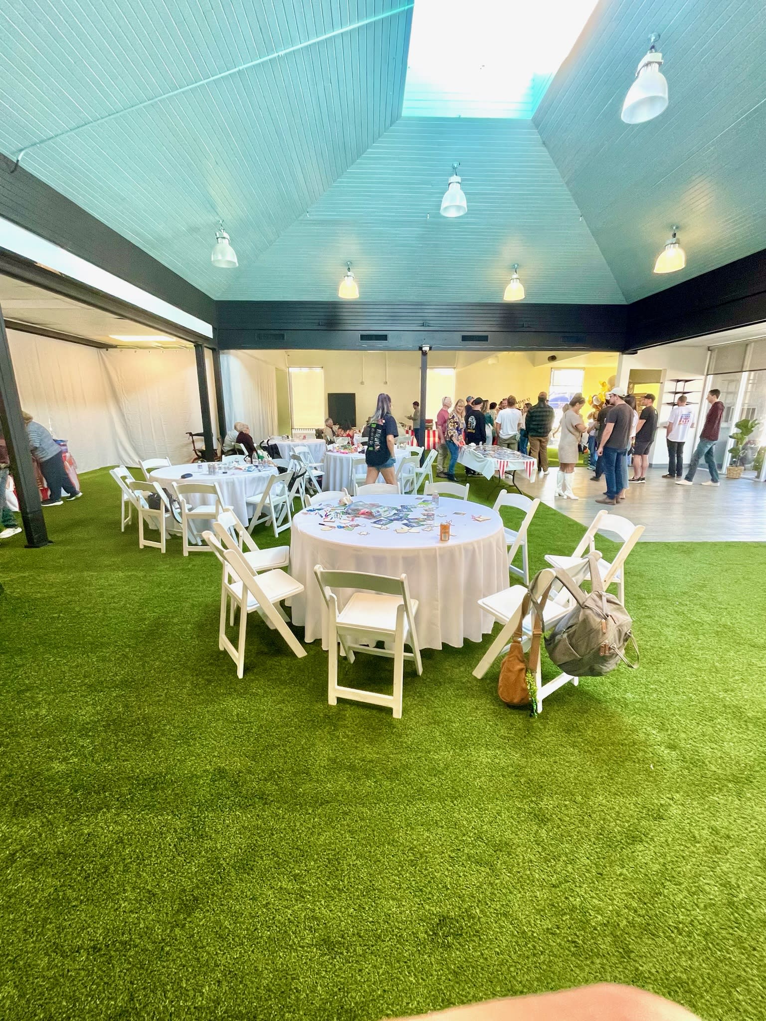 A lively private party takes place outdoors, with guests mingling, enjoying food, and dancing under string lights and palm trees.