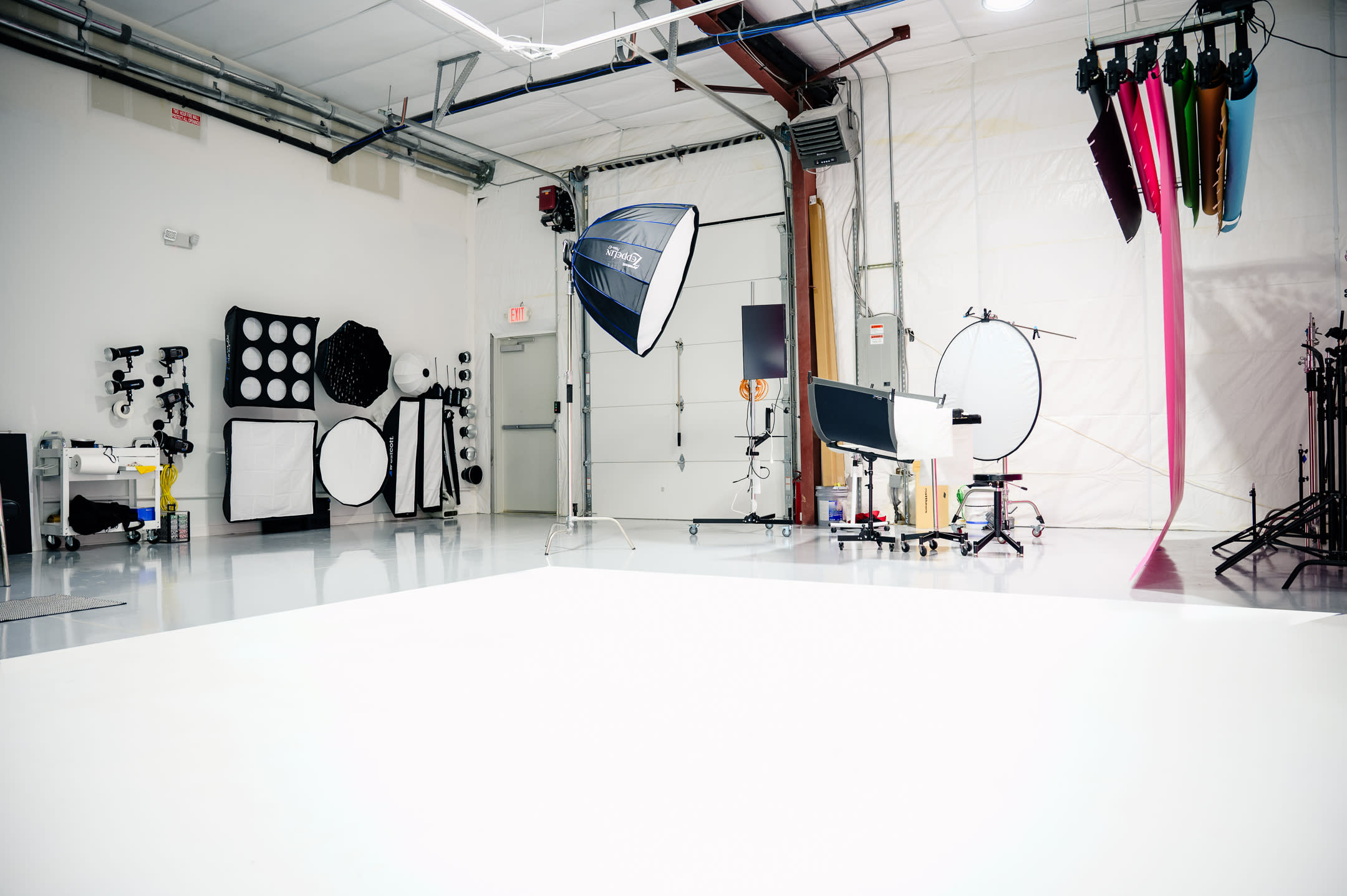 A man adjusts a large softbox light on a tripod in a spacious photography studio with a blank backdrop.