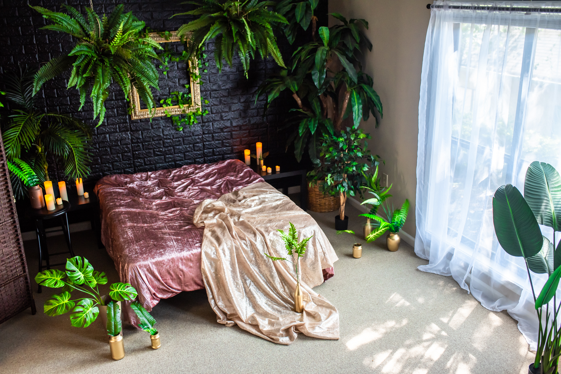 A model poses elegantly in lingerie, seated on the floor next to a fur throw in a dimly lit room with plants and candles.