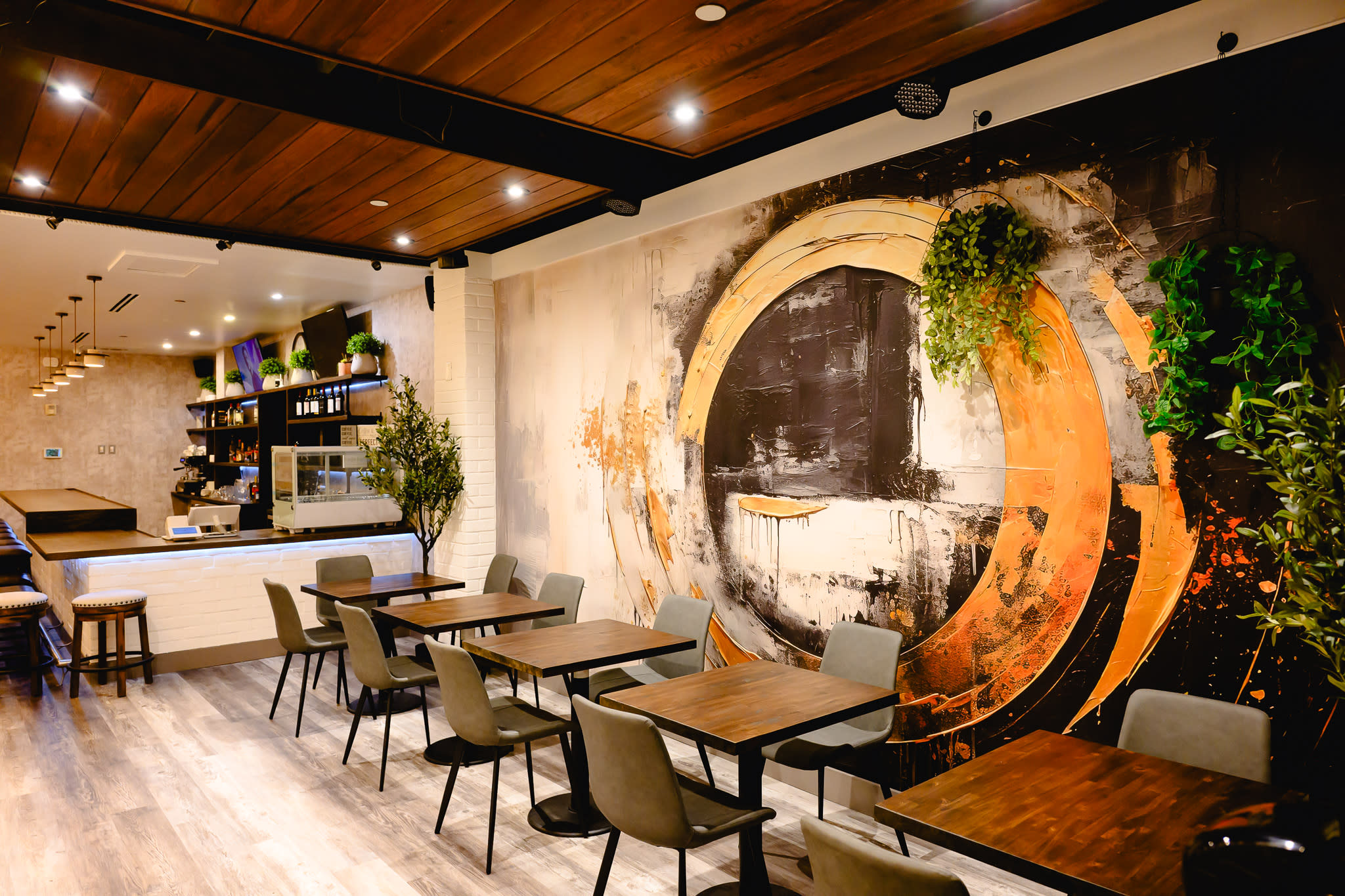 The image shows a modern reception area of a restaurant featuring a long bar with high stools and wooden tables arranged throughout the space.